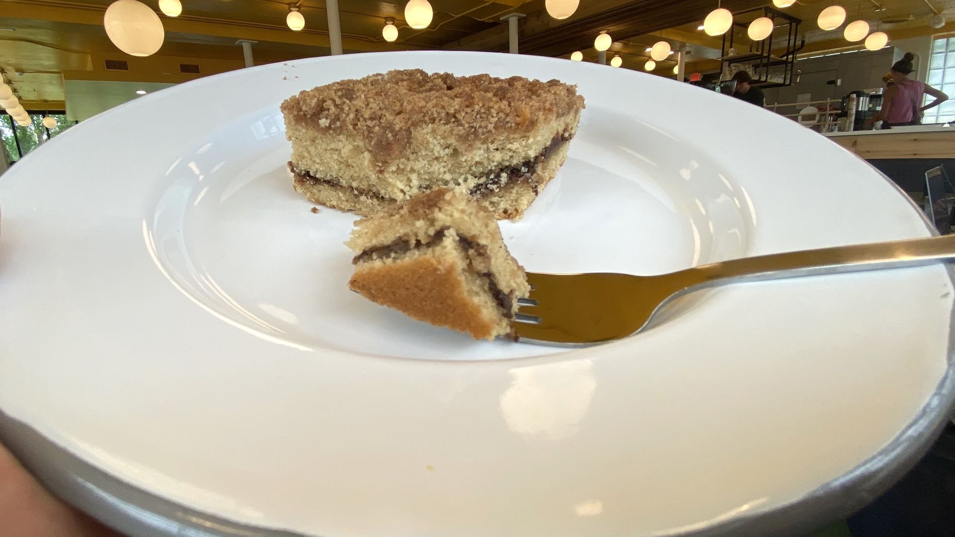 A piece of coffee cake on a white plate with a bite cut off and on a fork, ready to eat. 