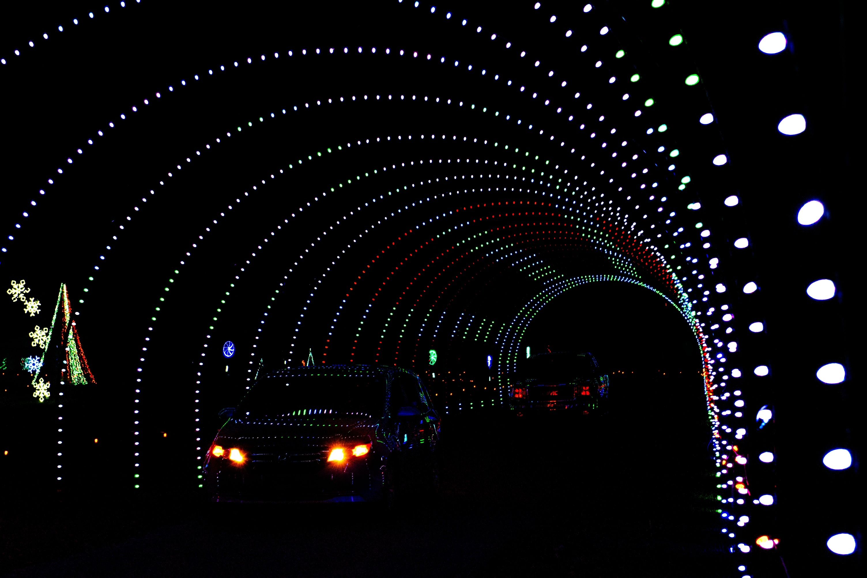 A car drives through a tunnel of Christmas lights illuminating the dark
