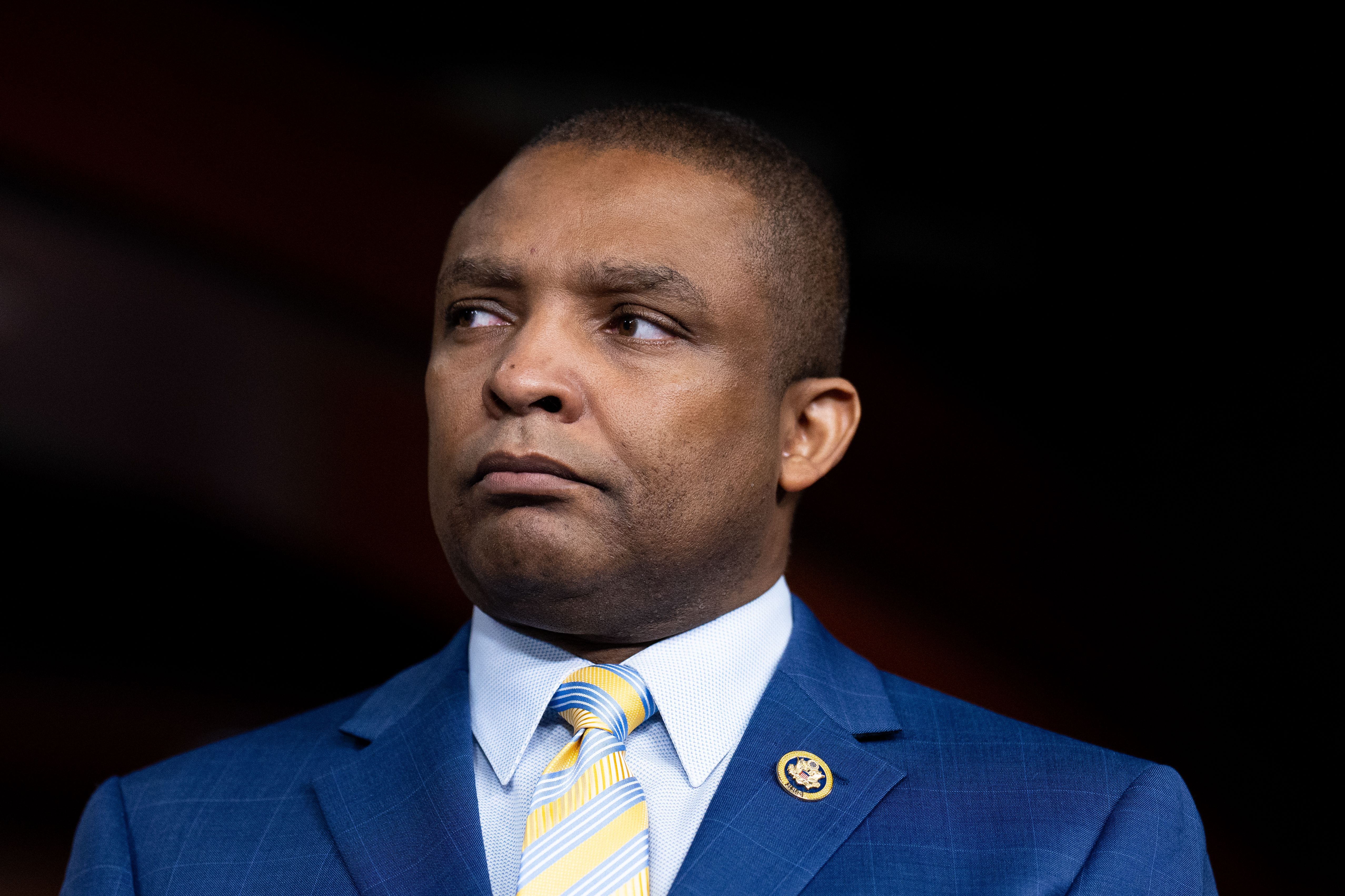 A congressman in a suit looks seriously to the right of the camera. It is a tight shot against a black background.