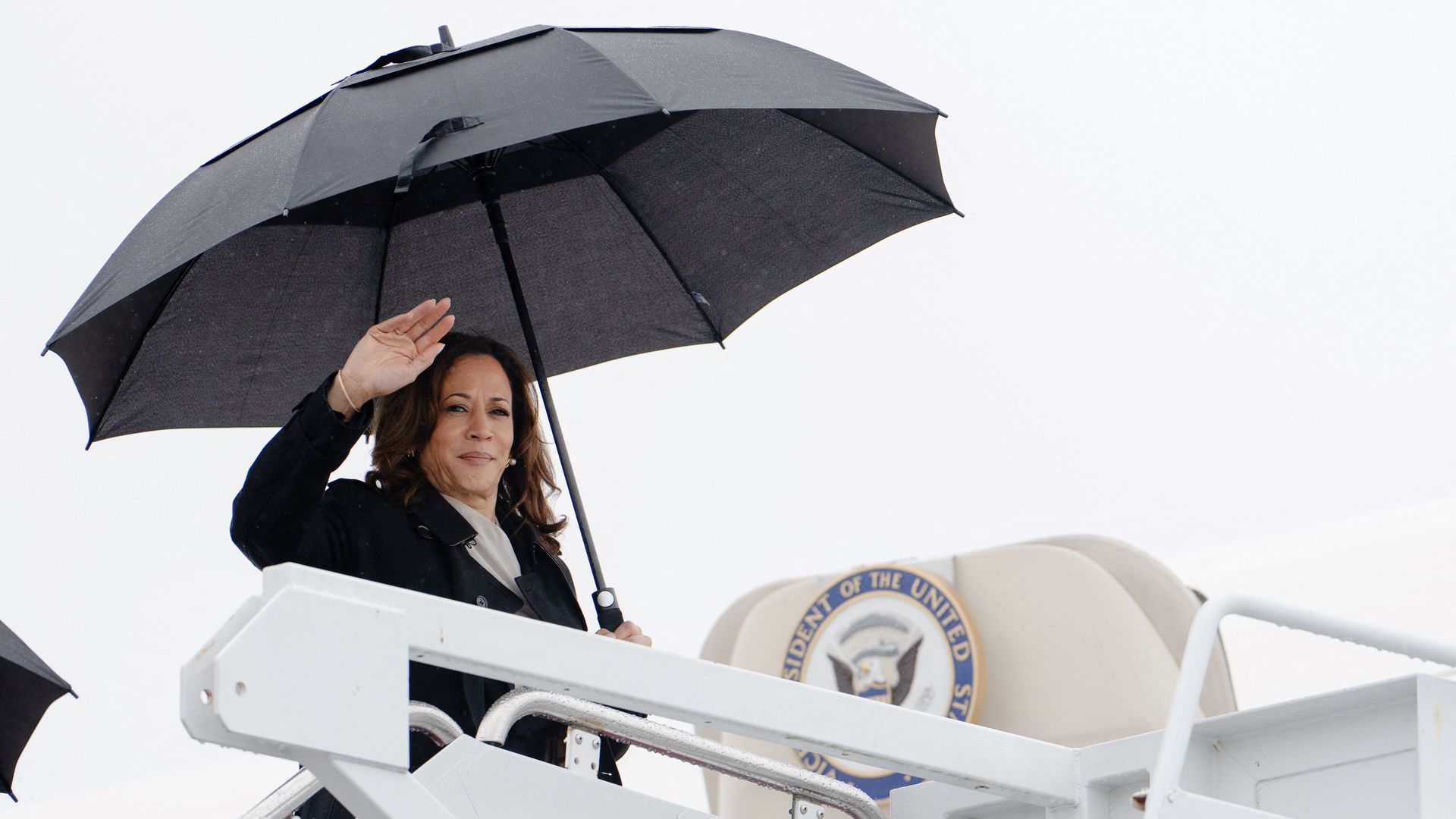 Vice President Harris holds an umbrella as she boards a plane.