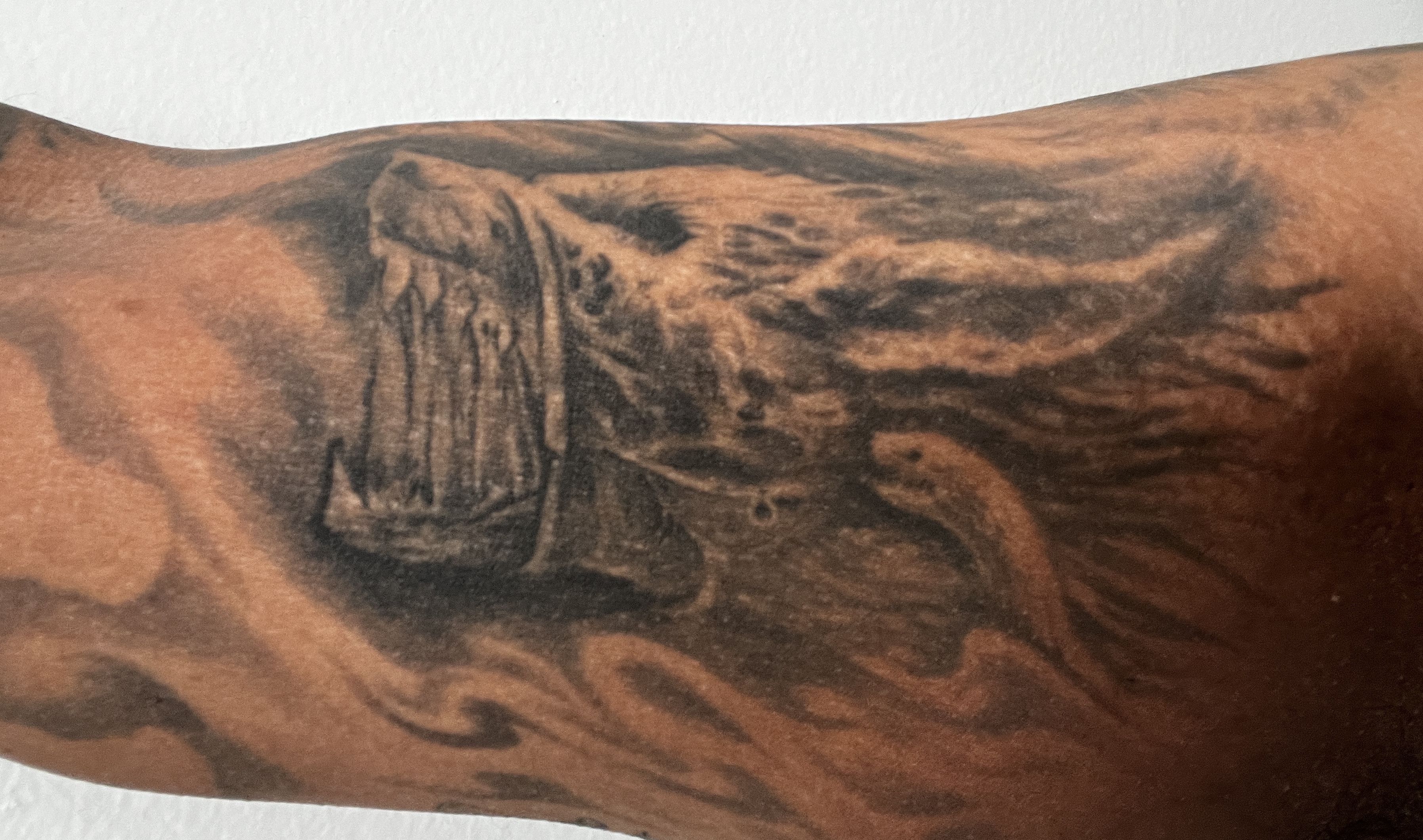 Black and gray tattoo of a roaring lion's head with detailed mane on an arm, surrounded by abstract shading and lines.