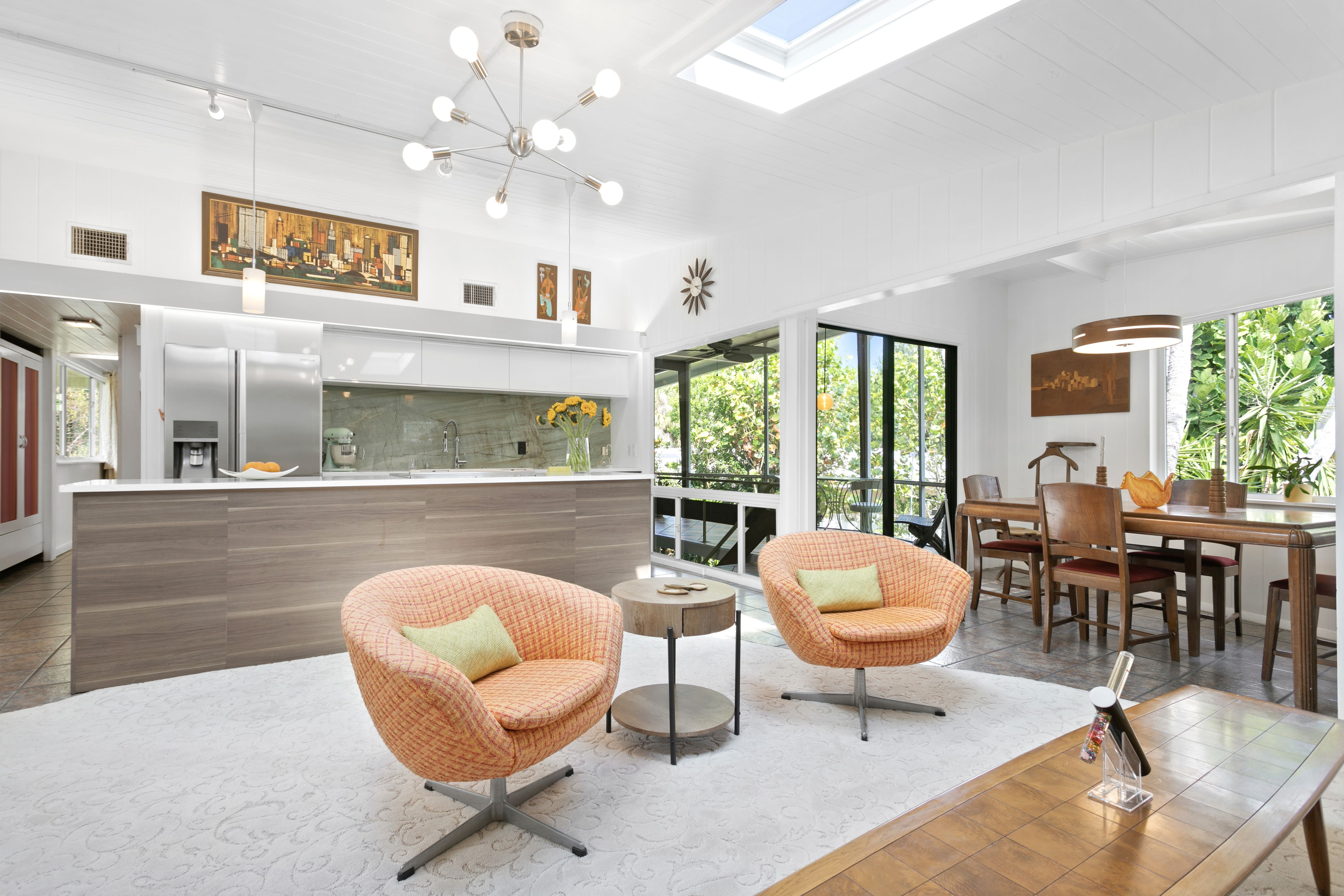 A living room with two orange chairs with a gray-and-white kitchen in the background.