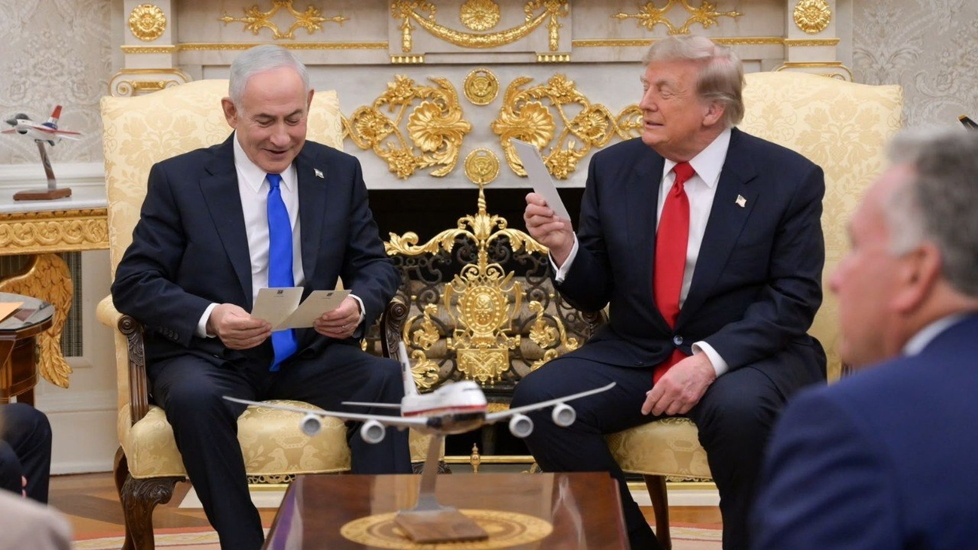 Israeli Prime Minister Benjamin Netanyahu and President Trump sit in the Oval Office holding cards, with model airplanes on a table in front of them.