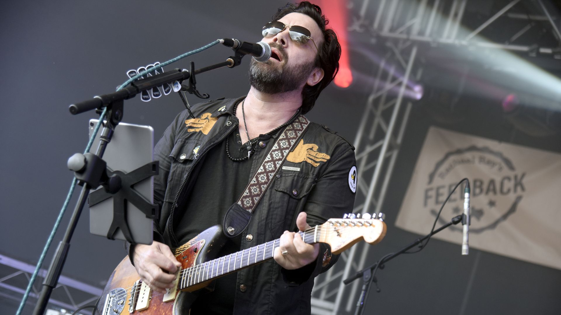 A photo of a musician singing into a mic while holding a guitar.