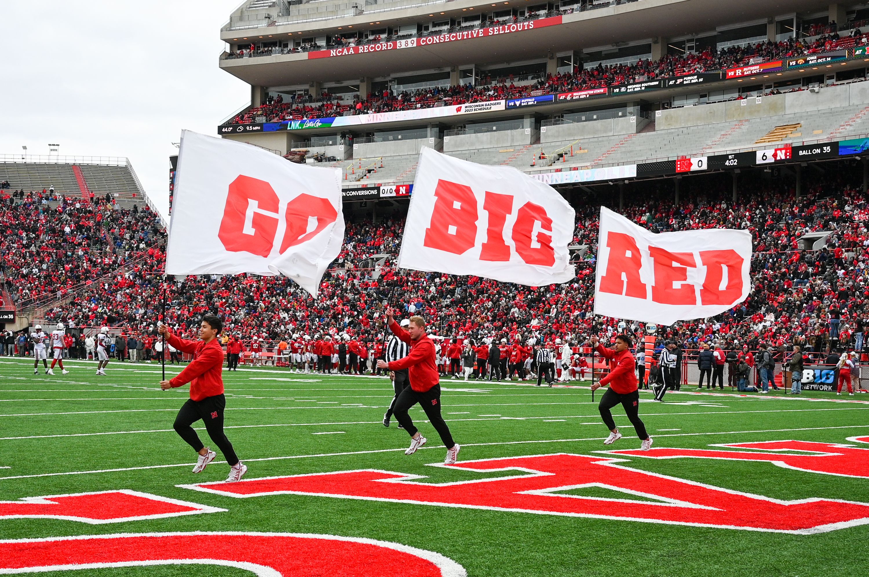 Photo of cheerleaders waving Go Big Red flags on football field 