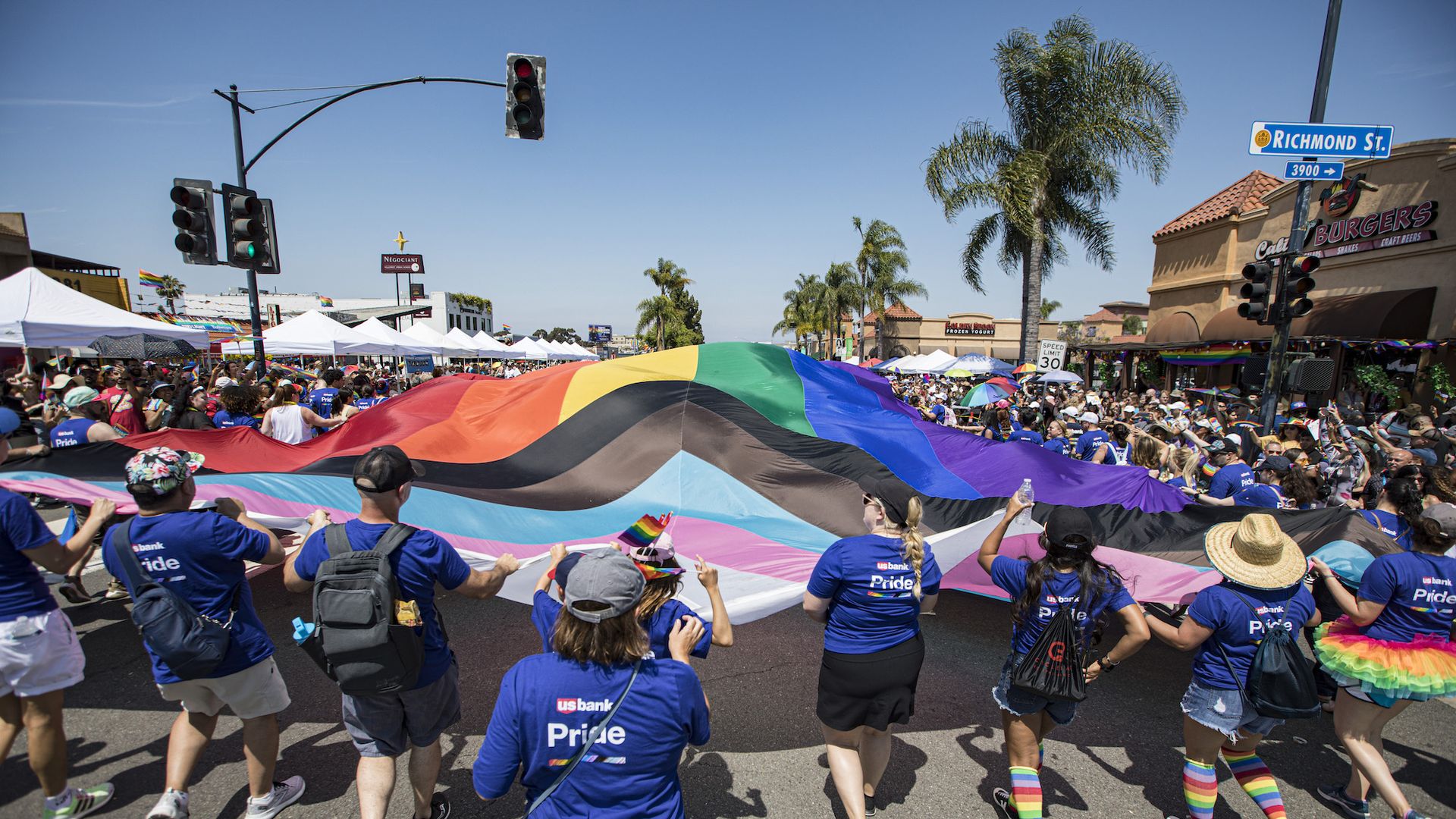 People march with a giant flag in a pride parade.