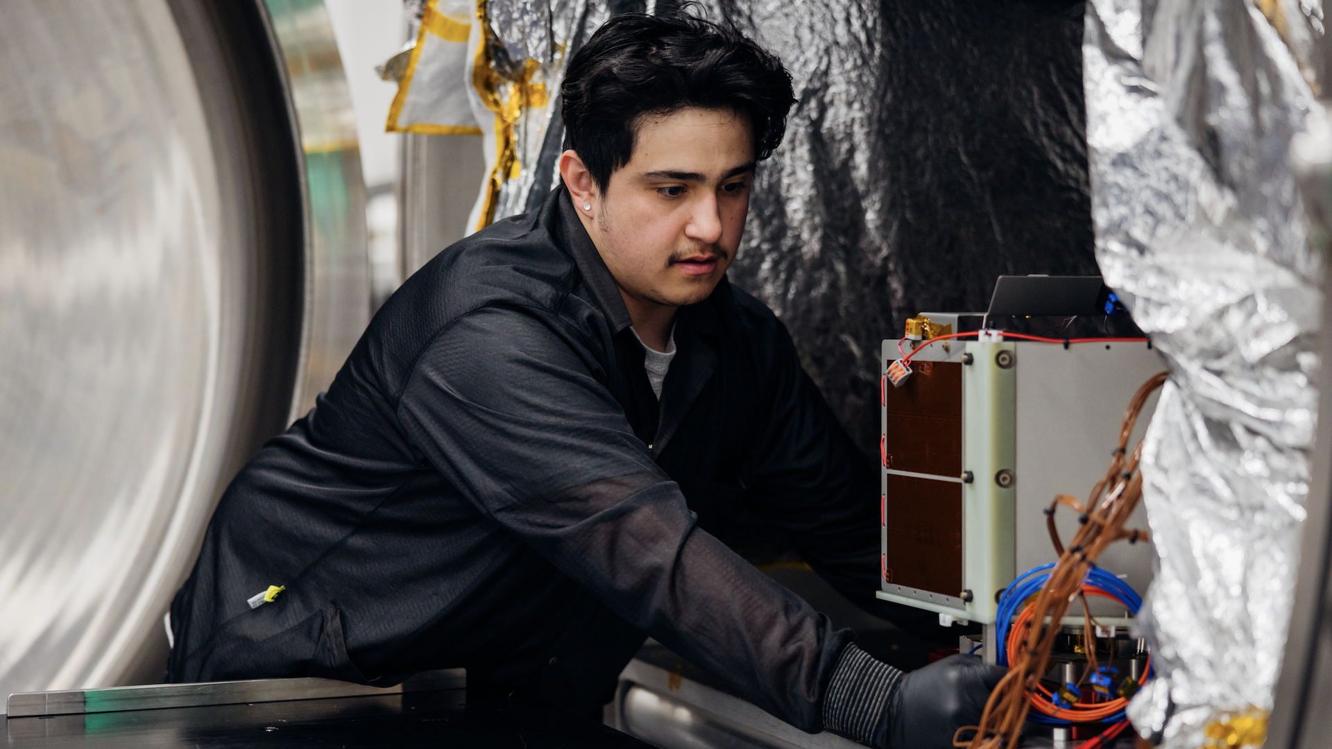 A young man in black works on satellite components. 