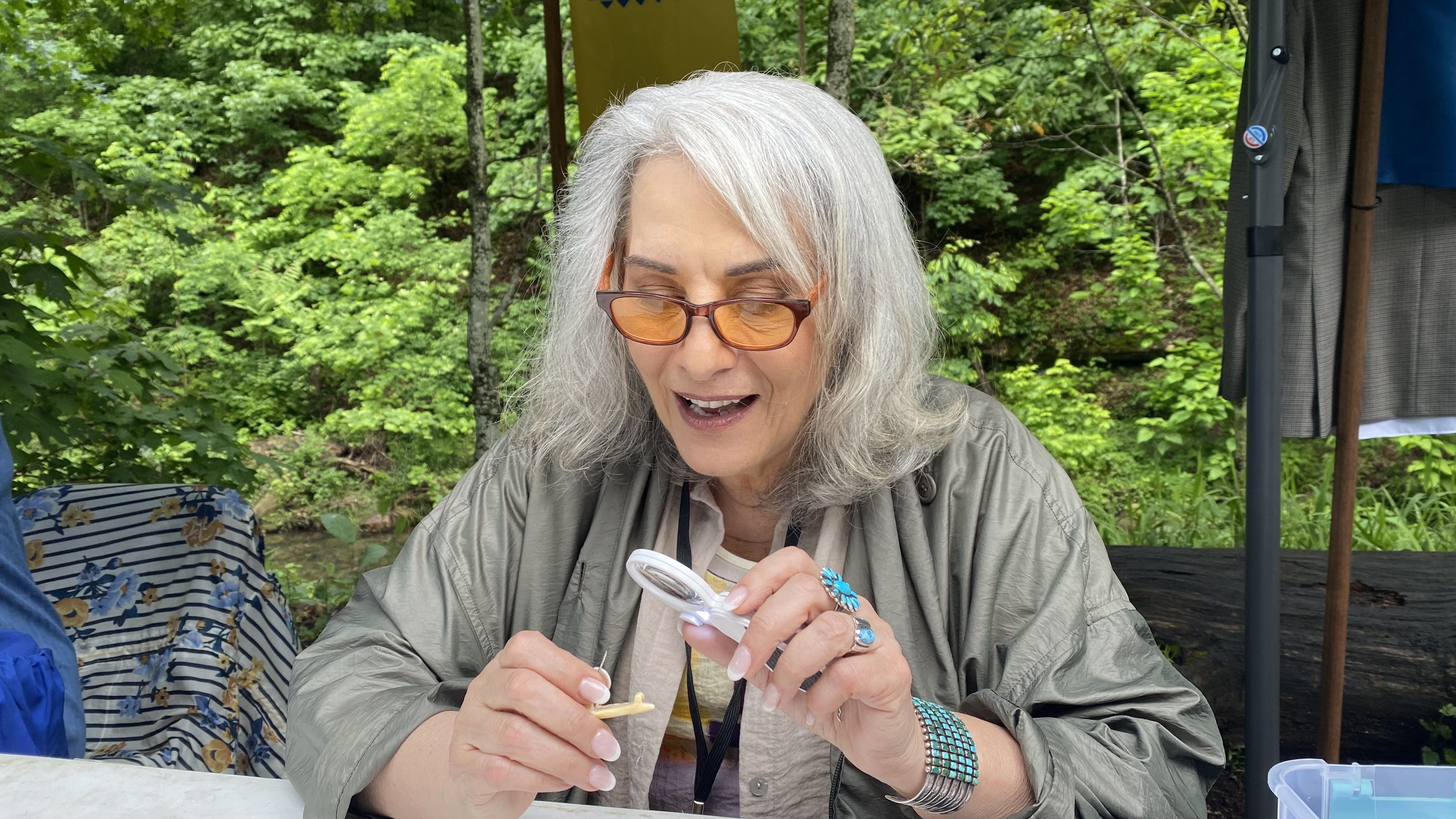 A photo of a woman inspecting a small piece of jewelry. 
