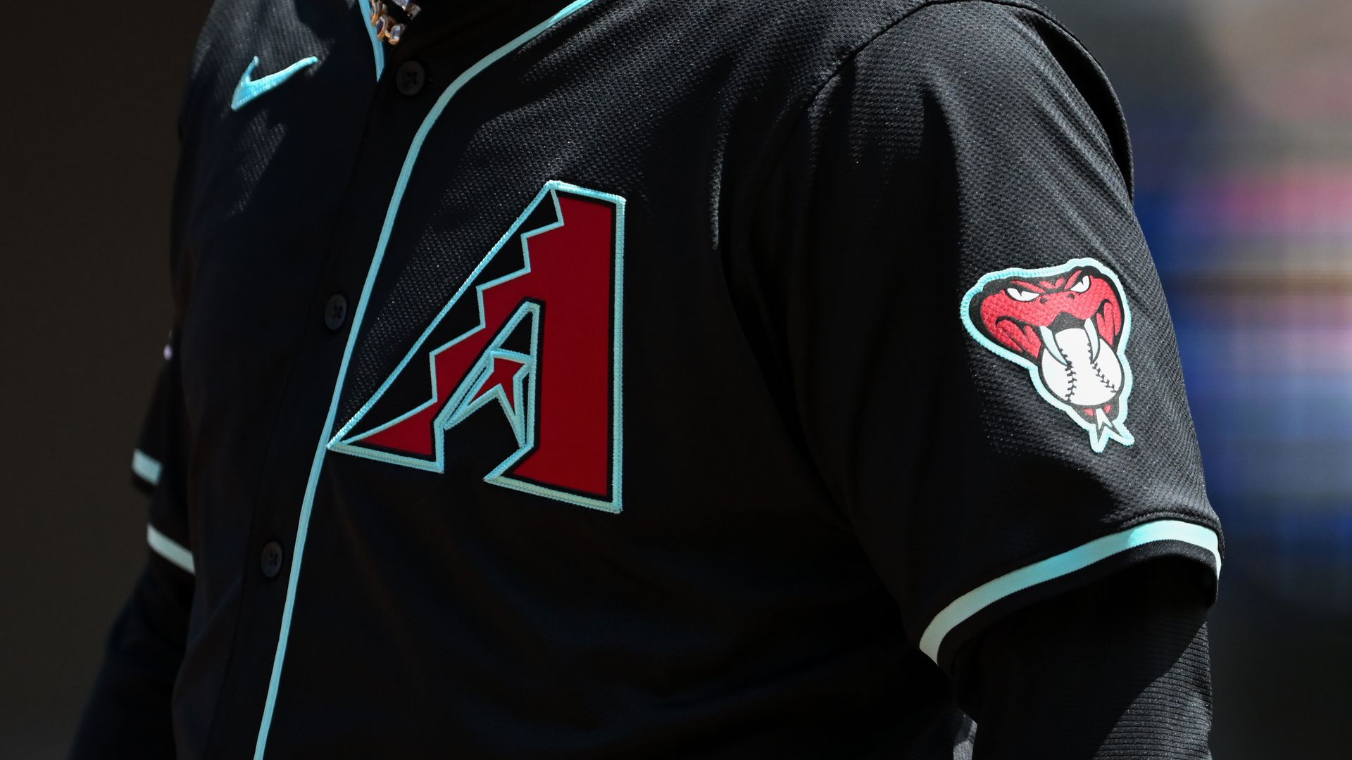 The front of a black baseball uniform with a red A logo with black and sky blue highlights on the left breast and a red snake holding a baseball in its mouth on the left sleeve. 