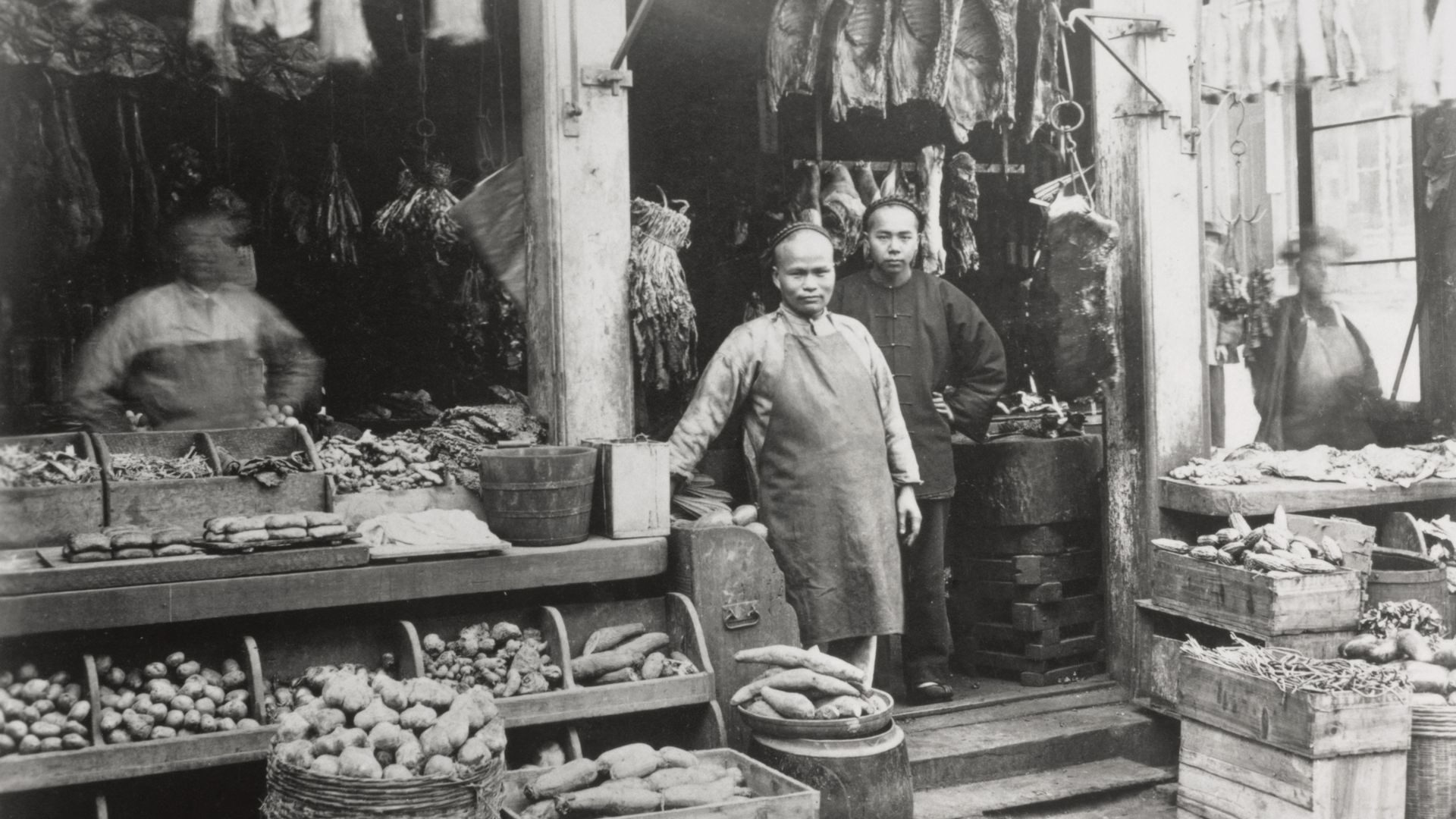 Black and white photo of Chinese people standing in front of an outdoor grocery market