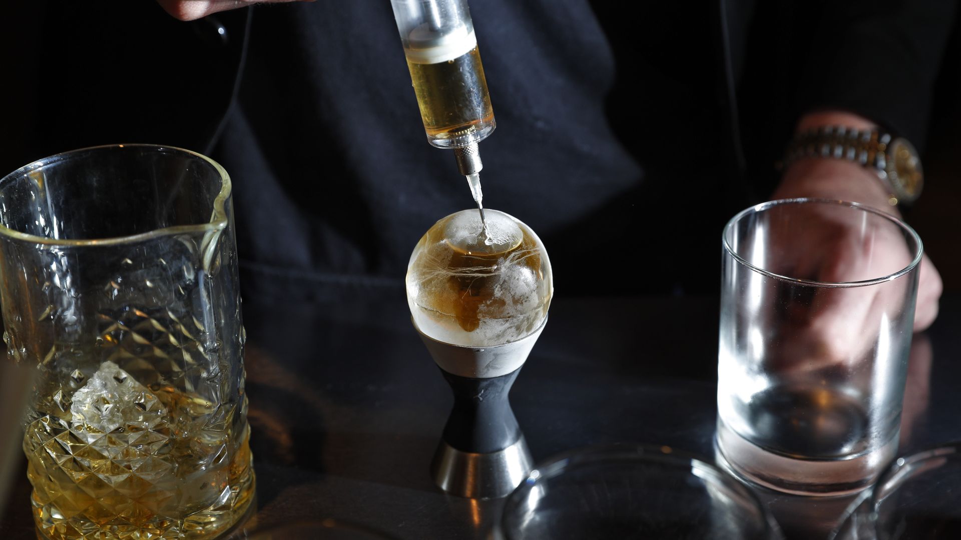 Photo of a bartender injecting a spirit into a hollow sphere of ice 