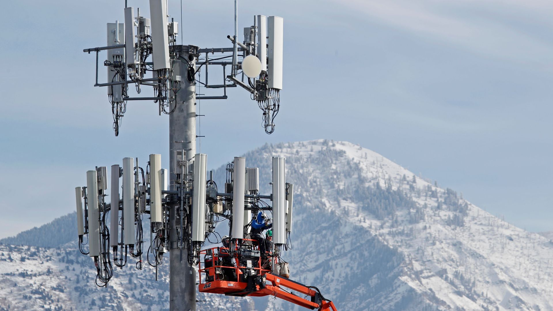 Photo of a cell tower with a crane working on it looming over a snowy mountain