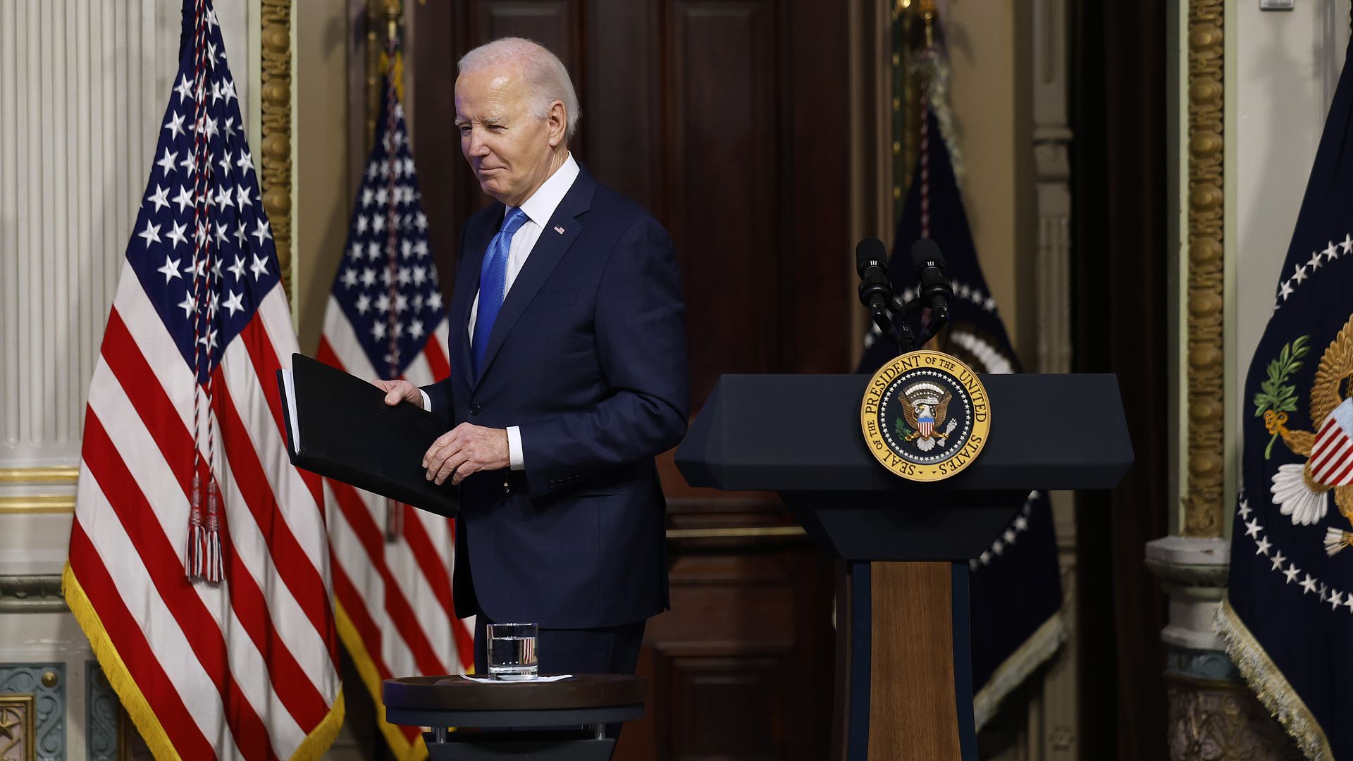 Biden walks behind a lectern with the American flag behind him.