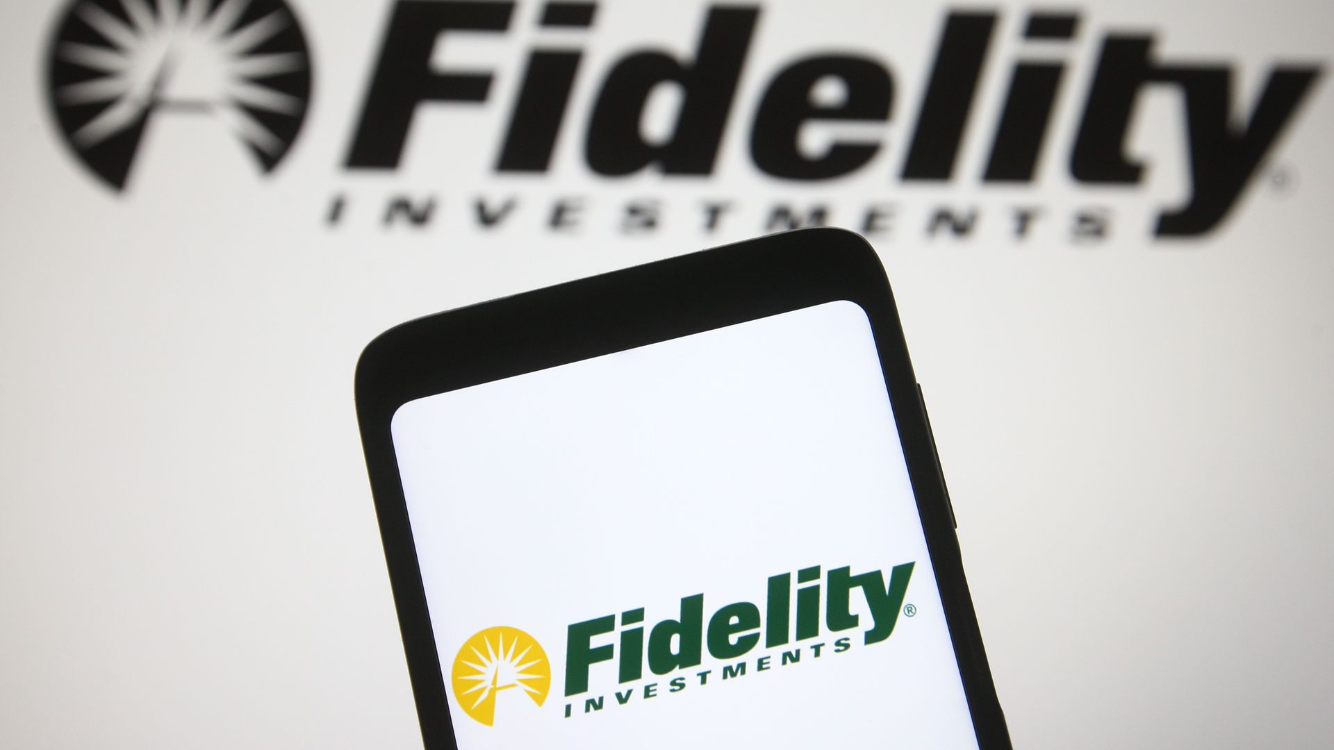 An iPhone is held in front of a Fidelity Investments logo. 