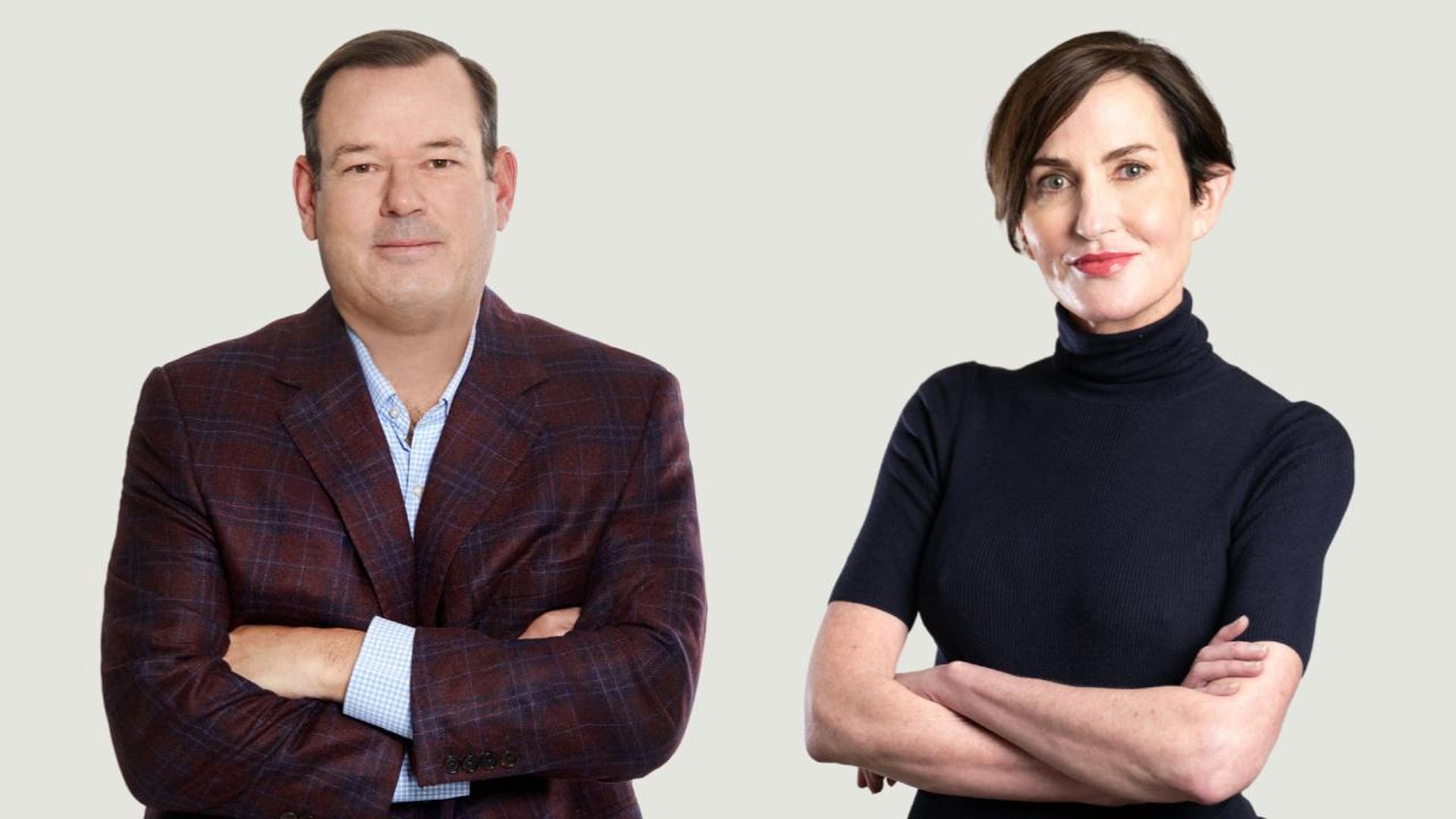 Man in a burgundy plaid blazer and light blue shirt and woman in a black turtleneck, both with arms crossed, posing against a light gray background.