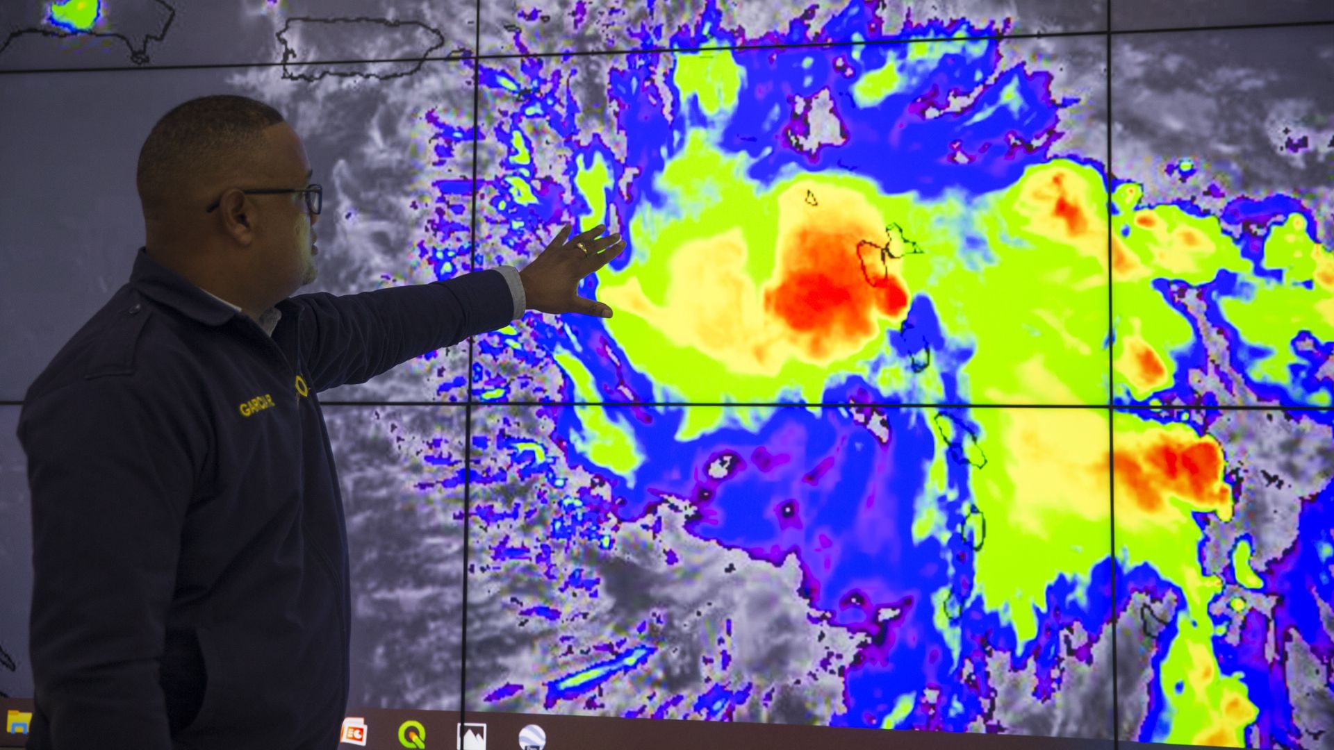 In this image, a man outstretches a hand towards a weather map that shows a tropical storm in different colors