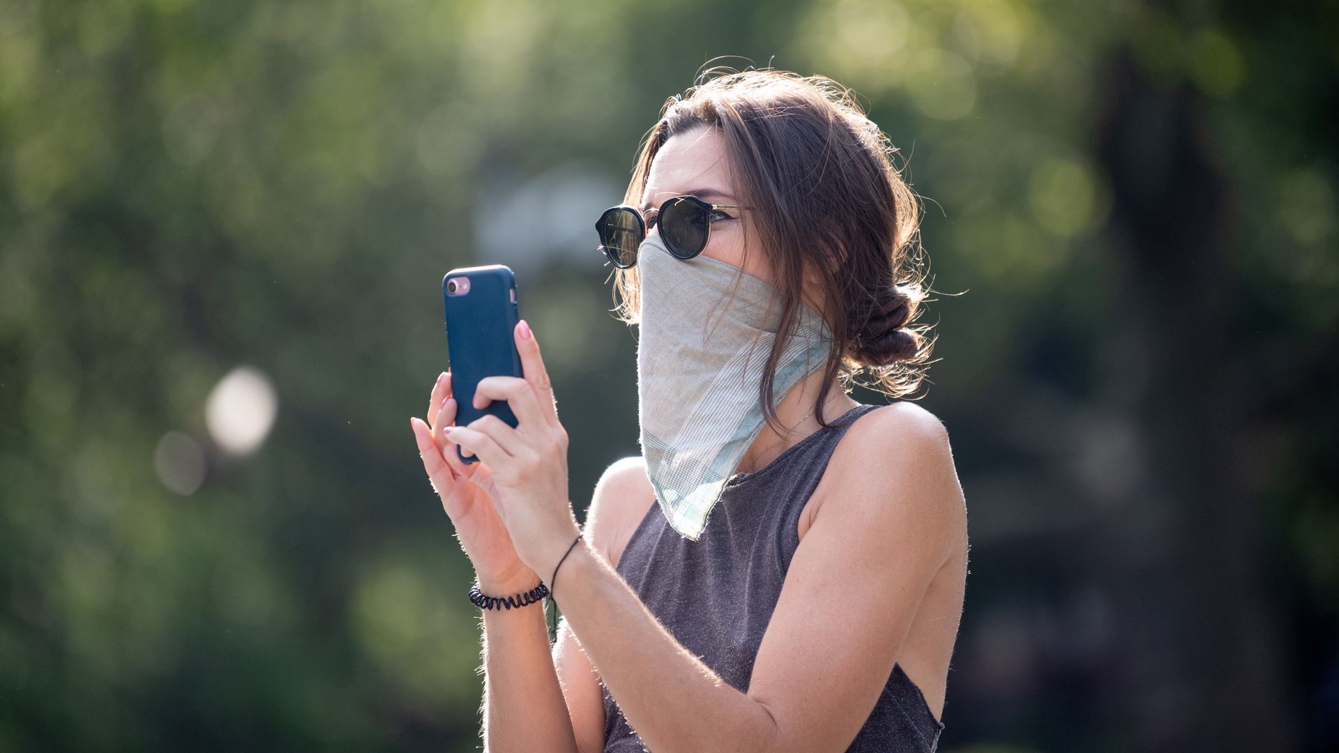 A photo of a woman in a face mask using an iPhone.