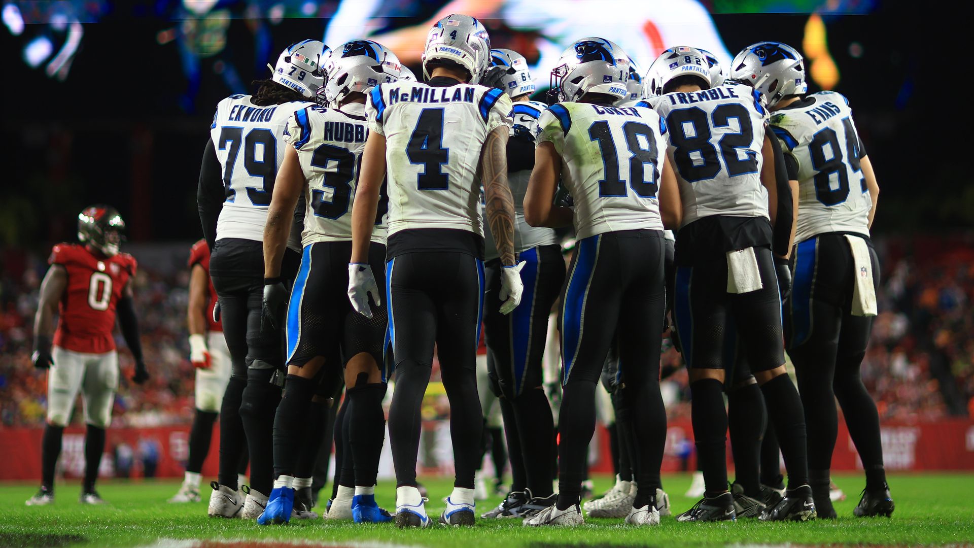 Panthers players huddle in white jerseys, silver helmets and black pants. 