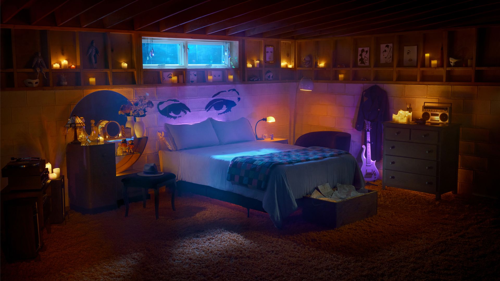 A basement bedroom with blue light shining through a window near the ceiling over a bed with eyes painted over the head and purple tinting around the room.