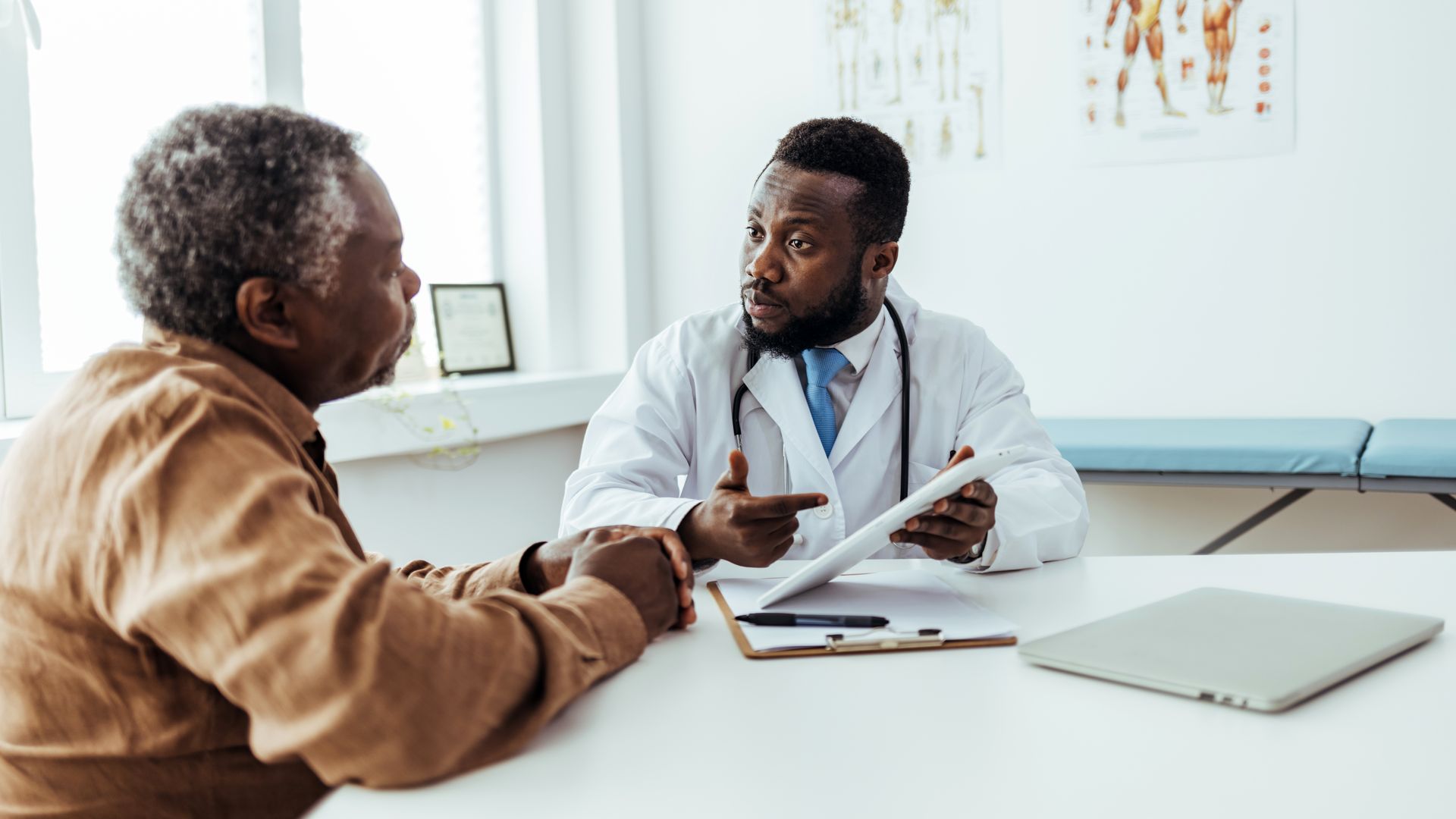A male doctor and a man are talking at a table. 