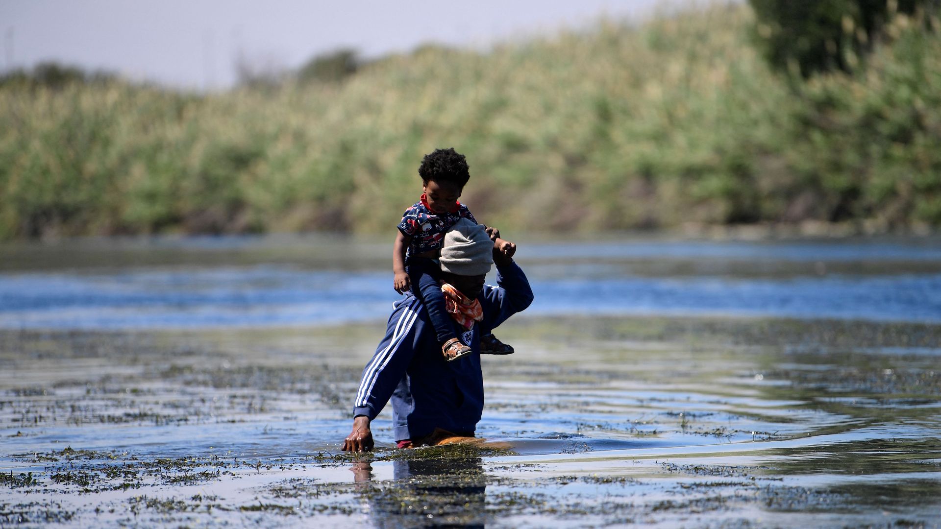 A Haitian migrant is seen carrying a toddler on his shoulders as he crossed the Rio Grande River.