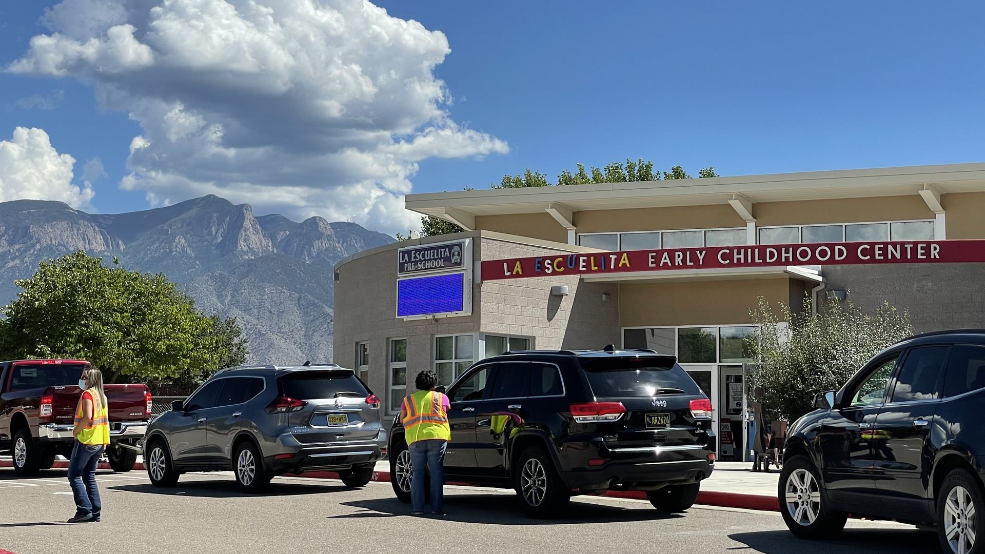 Parents wait in line to pick up preschoolers from a New Mexico school with the Sandia Mountains in the background.