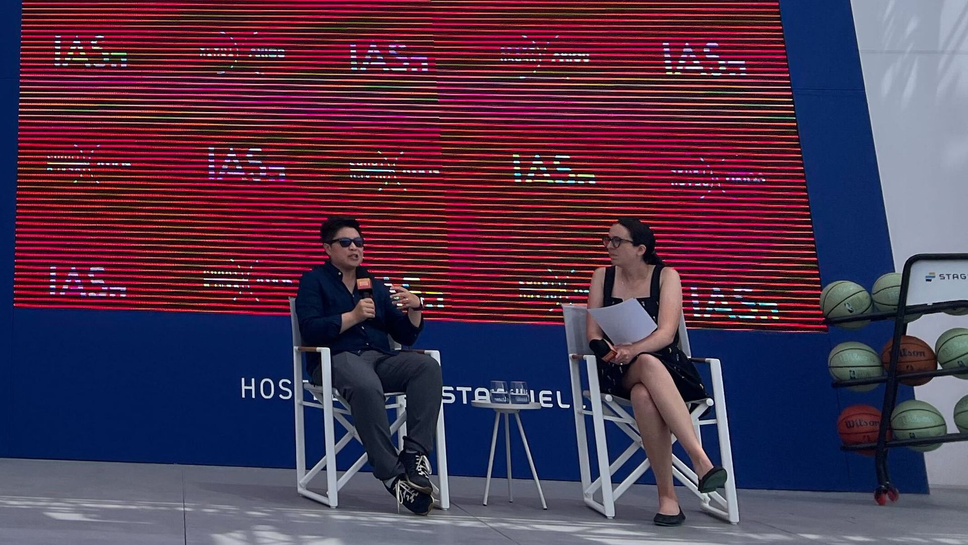 Jen Wong and Kerry Flynn sitting in white chairs on a stage next to a bunch of basketballs