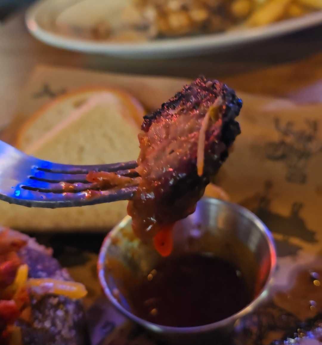 A fork holds a piece of brisket over a tin of barbecue sauce.