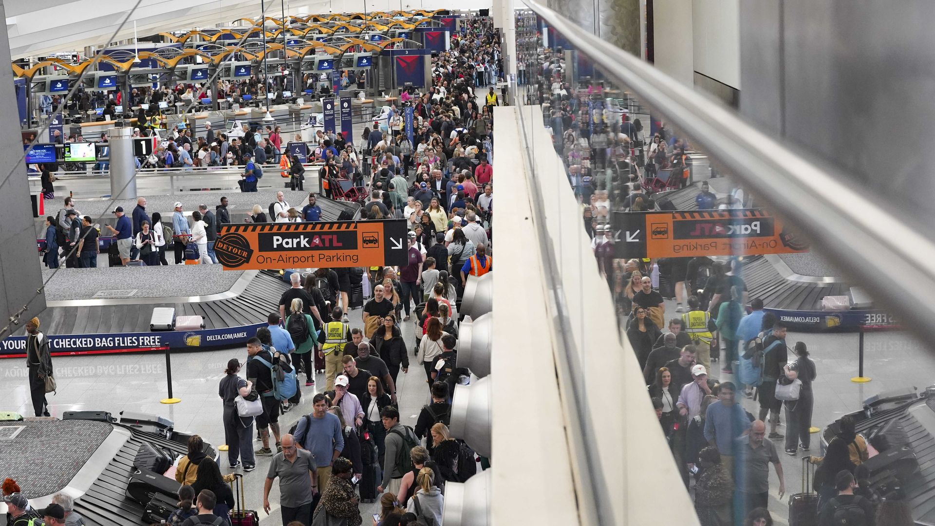 Hundreds of people stand in long TSA screening lines stretching through an airport's baggage claim and check-in area.