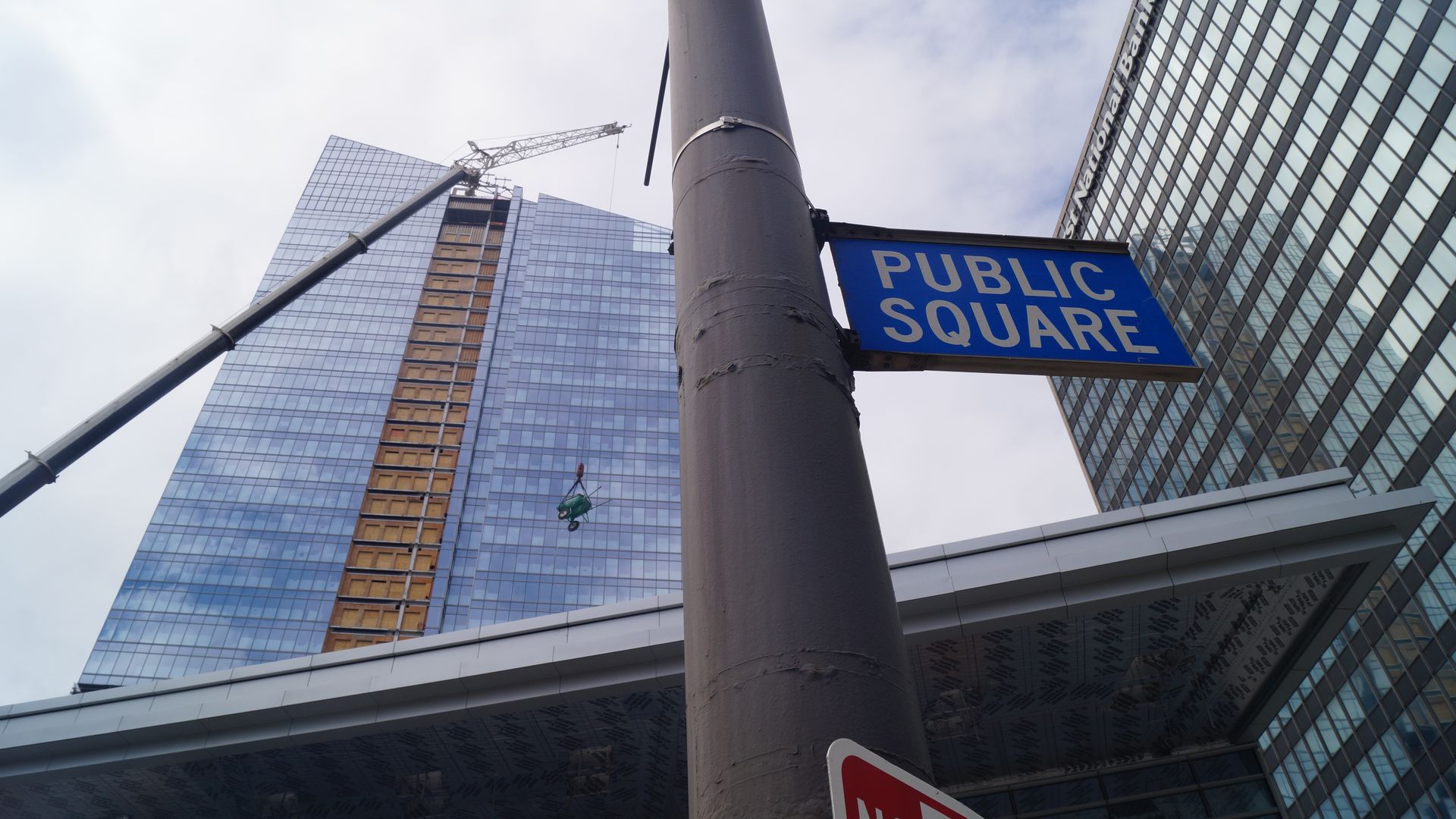 An image of a new skyscraper behind a pole with "Public Square" street sign in blue