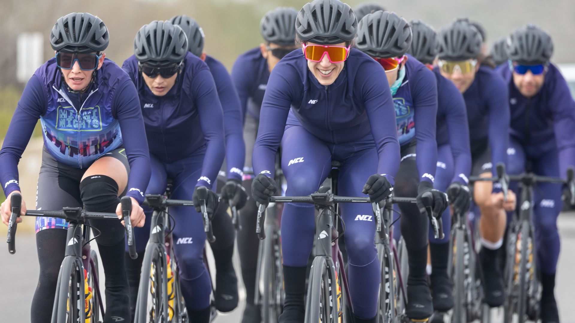 A pack of cyclists in dark blue rides close together 