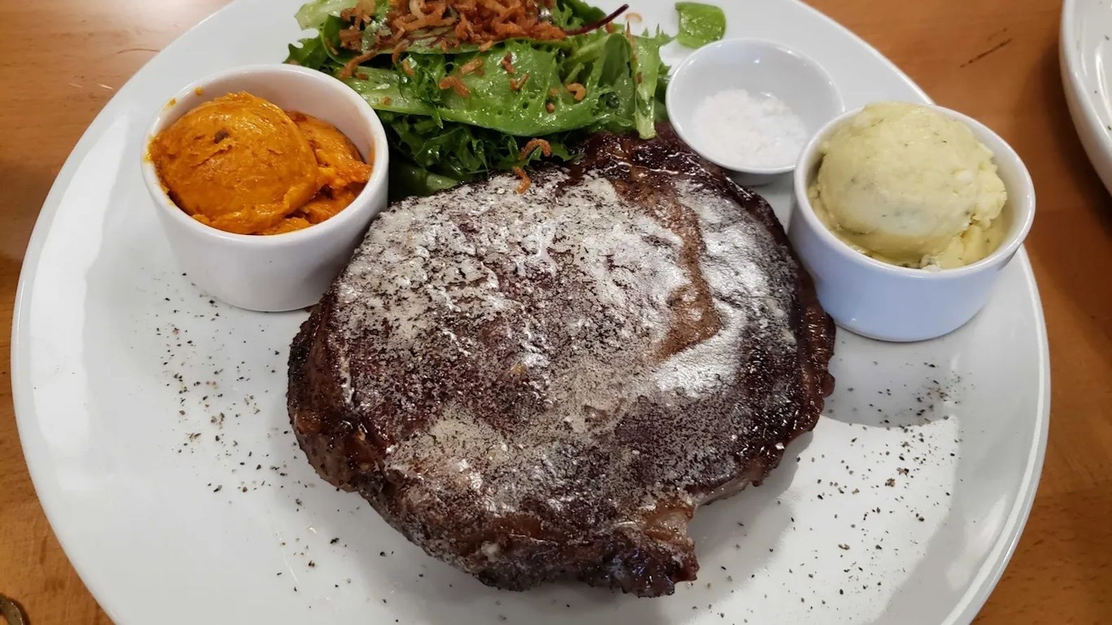 Photo of a plate of food featuring a big steak with mashed potatoes and carrots