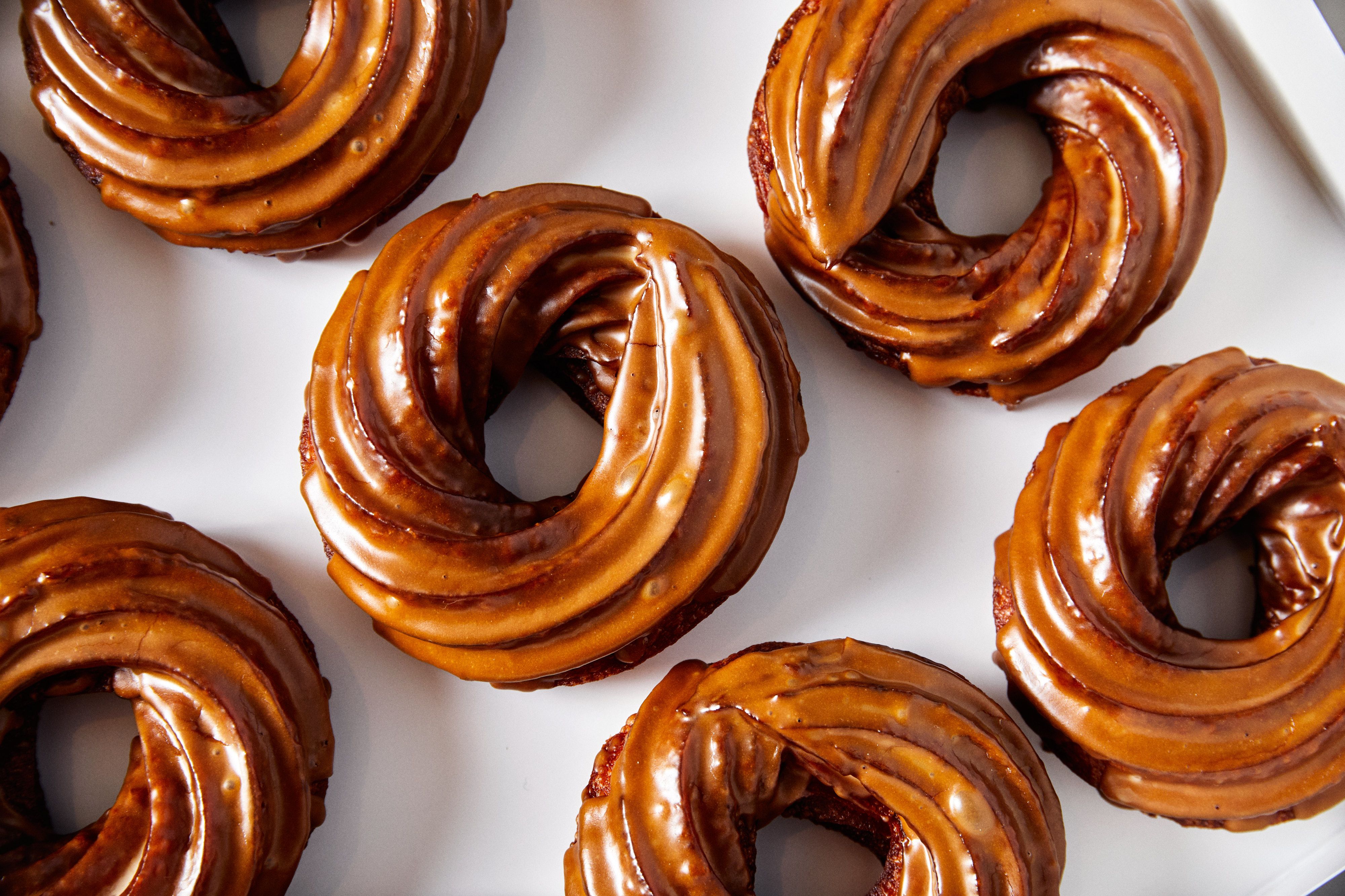Close-up of several chocolate-glazed cruller donuts arranged on a white surface with a shiny, smooth icing coating.