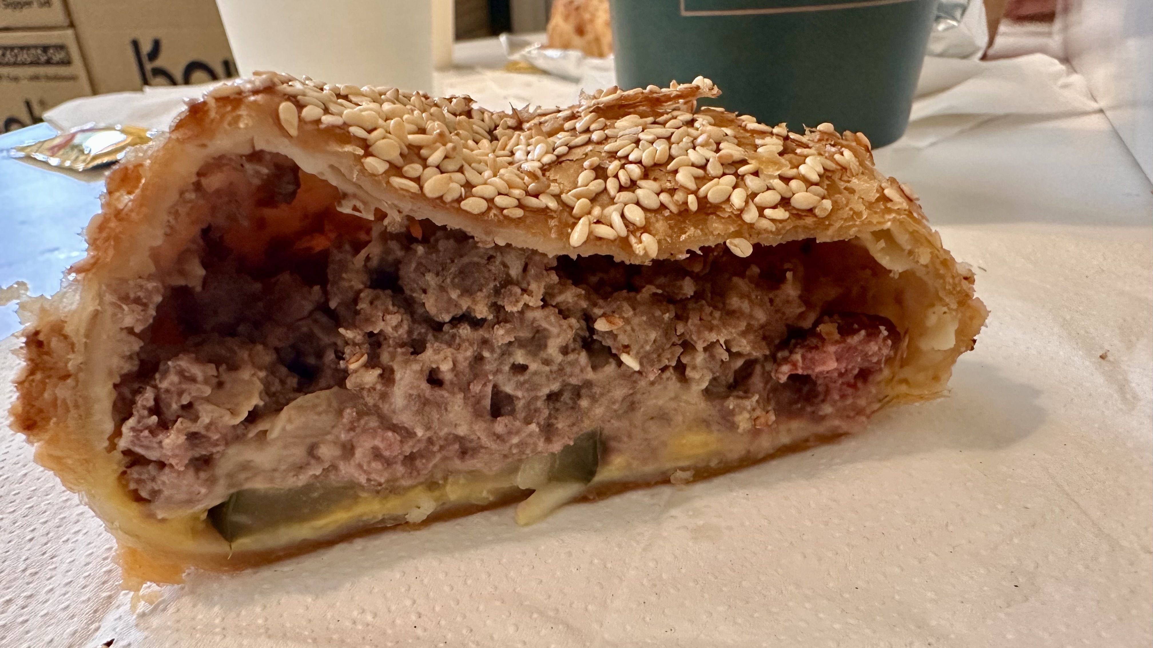 Close-up of a sesame-seed–topped savory pastry, flaky crust split open to reveal a dense ground meat filling