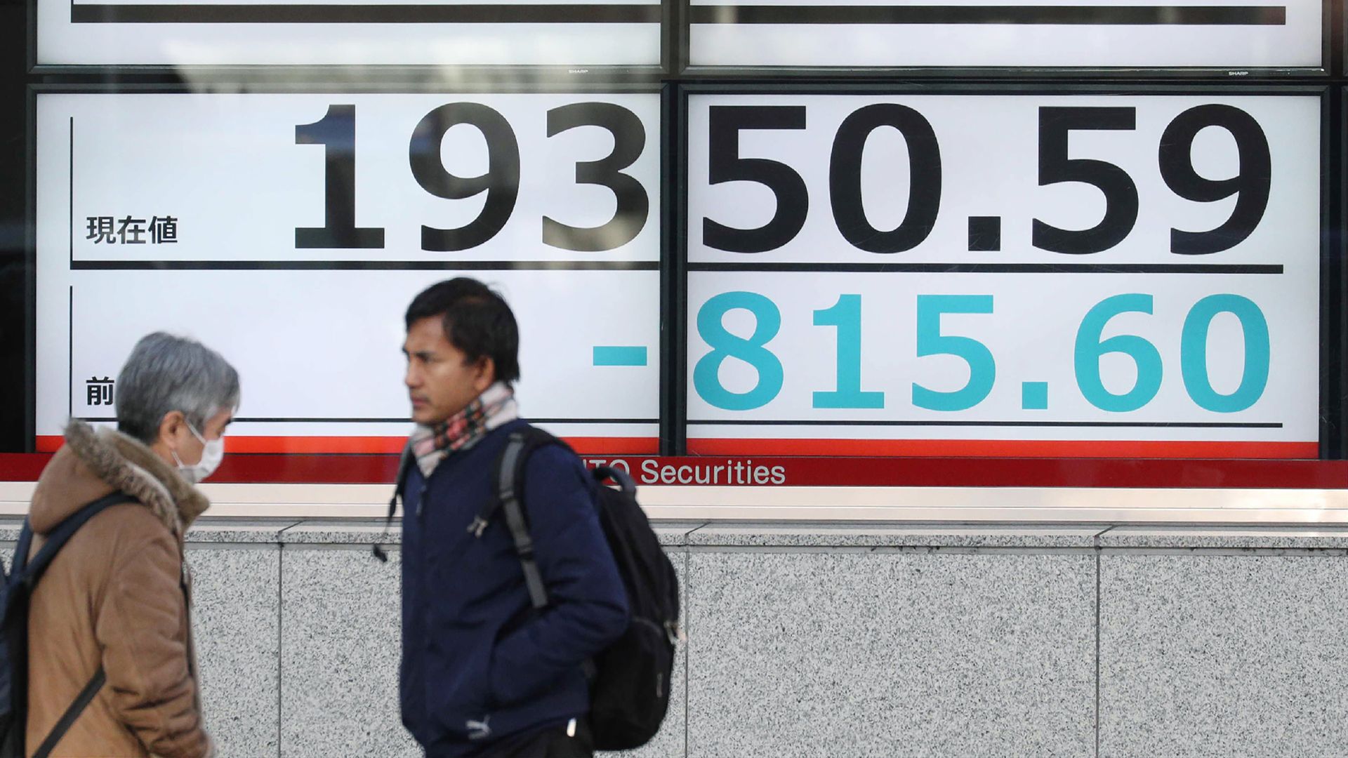 Pedestrians walk past a board showing the share price of the Tokyo Stock Exchange