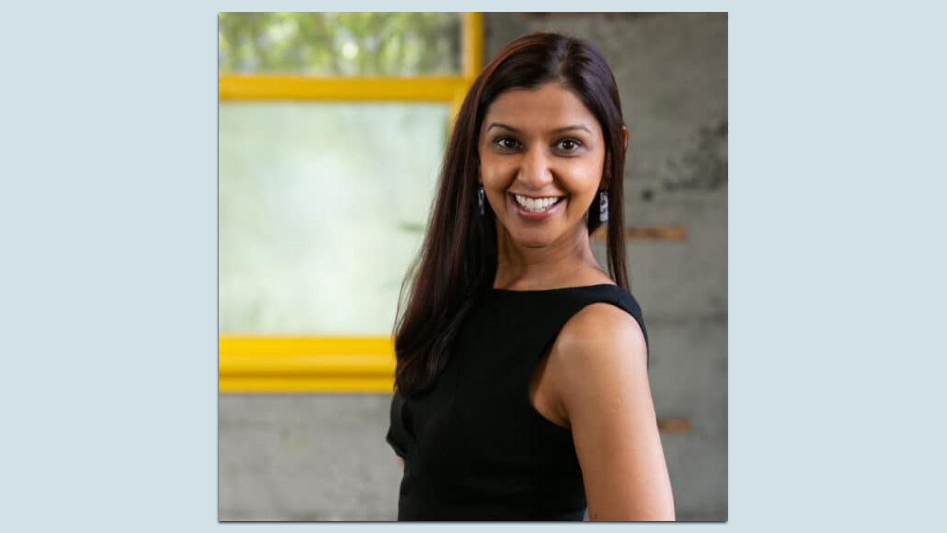 Purva Merchant smiles and looks at the camera in a headshot photo mounted on a light blue background.