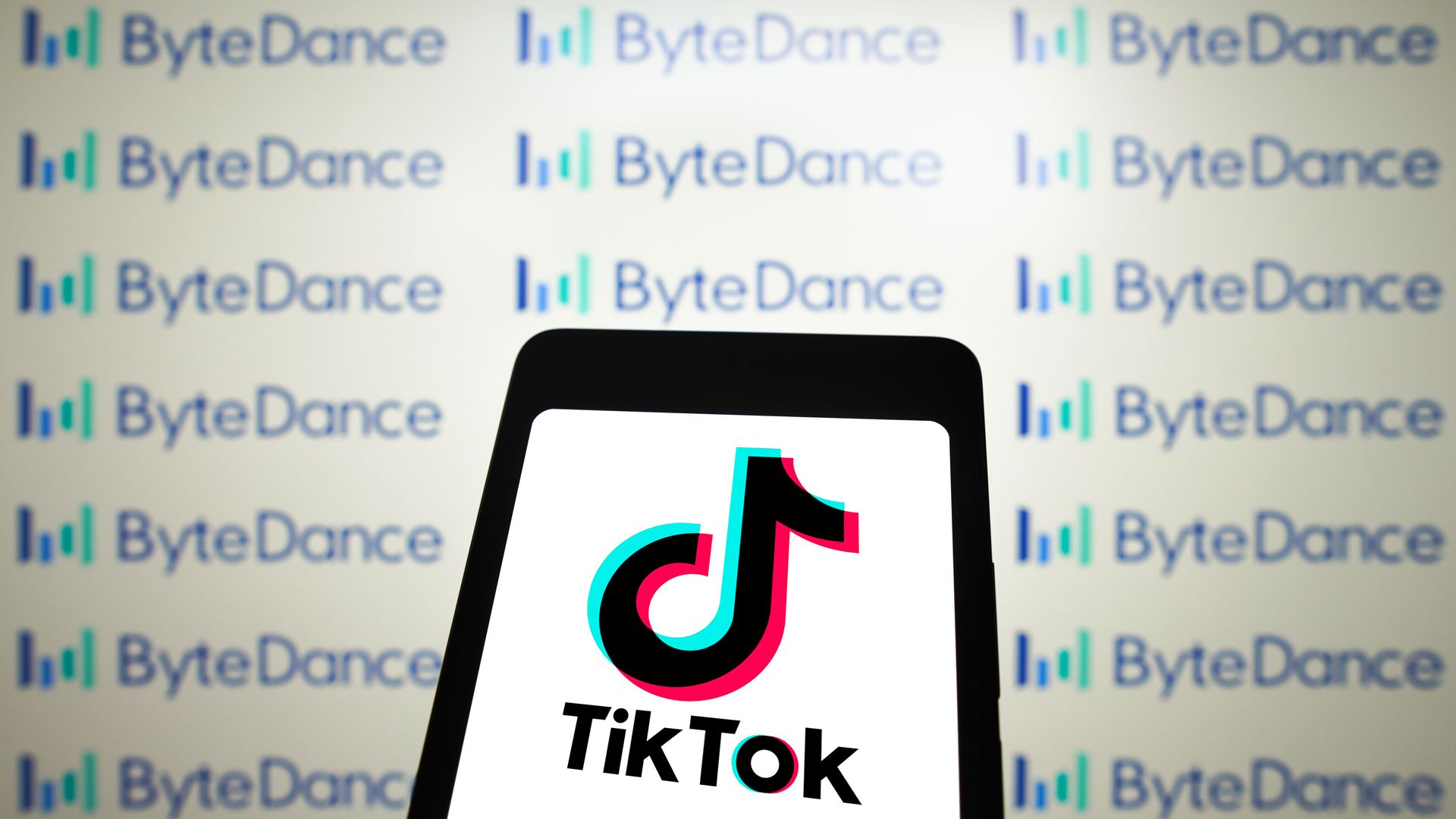In this photo illustration, the TikTok logo is displayed on a smartphone screen with the logo ByteDance in the background.