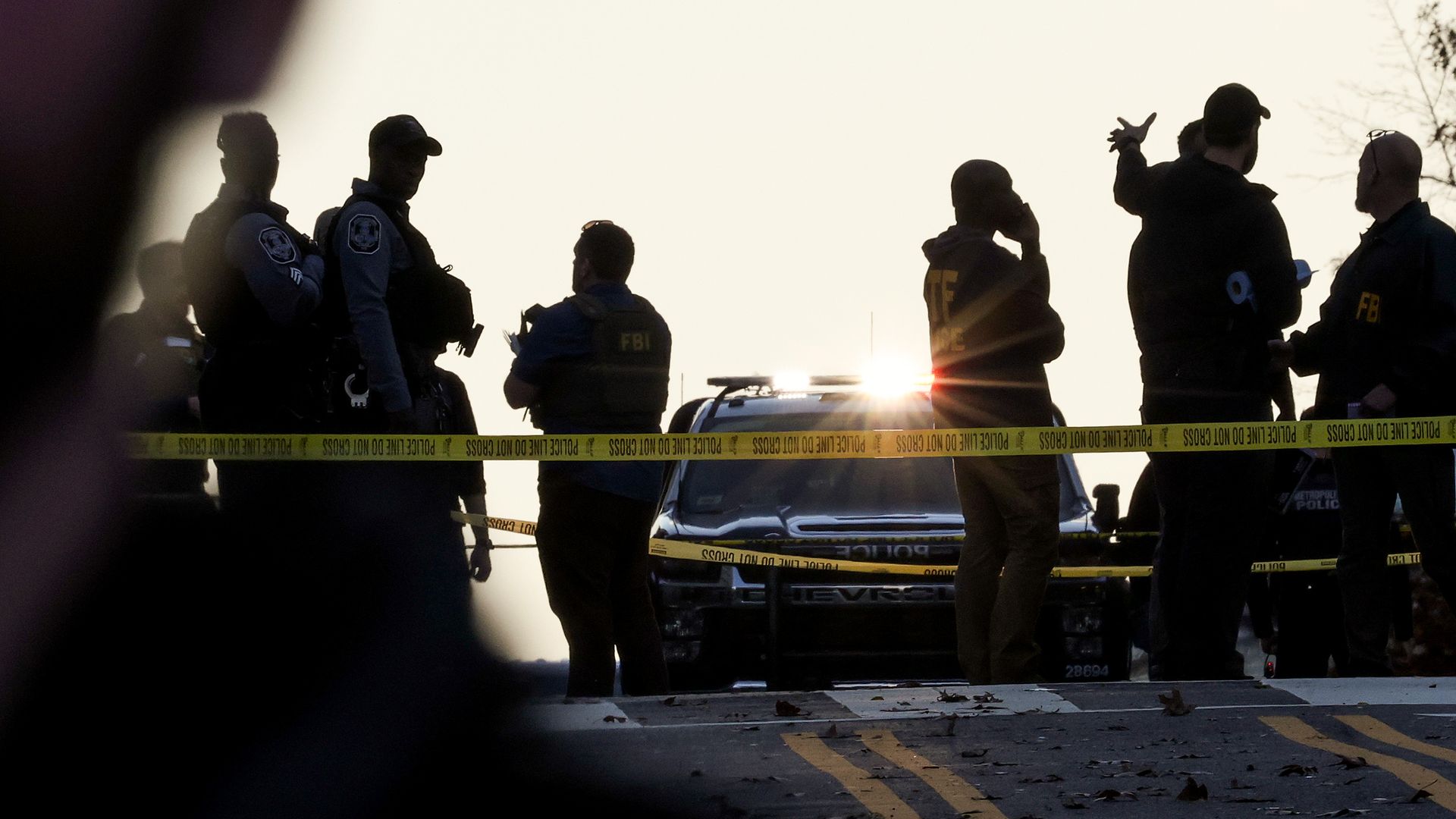 Members of law enforcement gather behind yellow crime tape on a D.C. road.