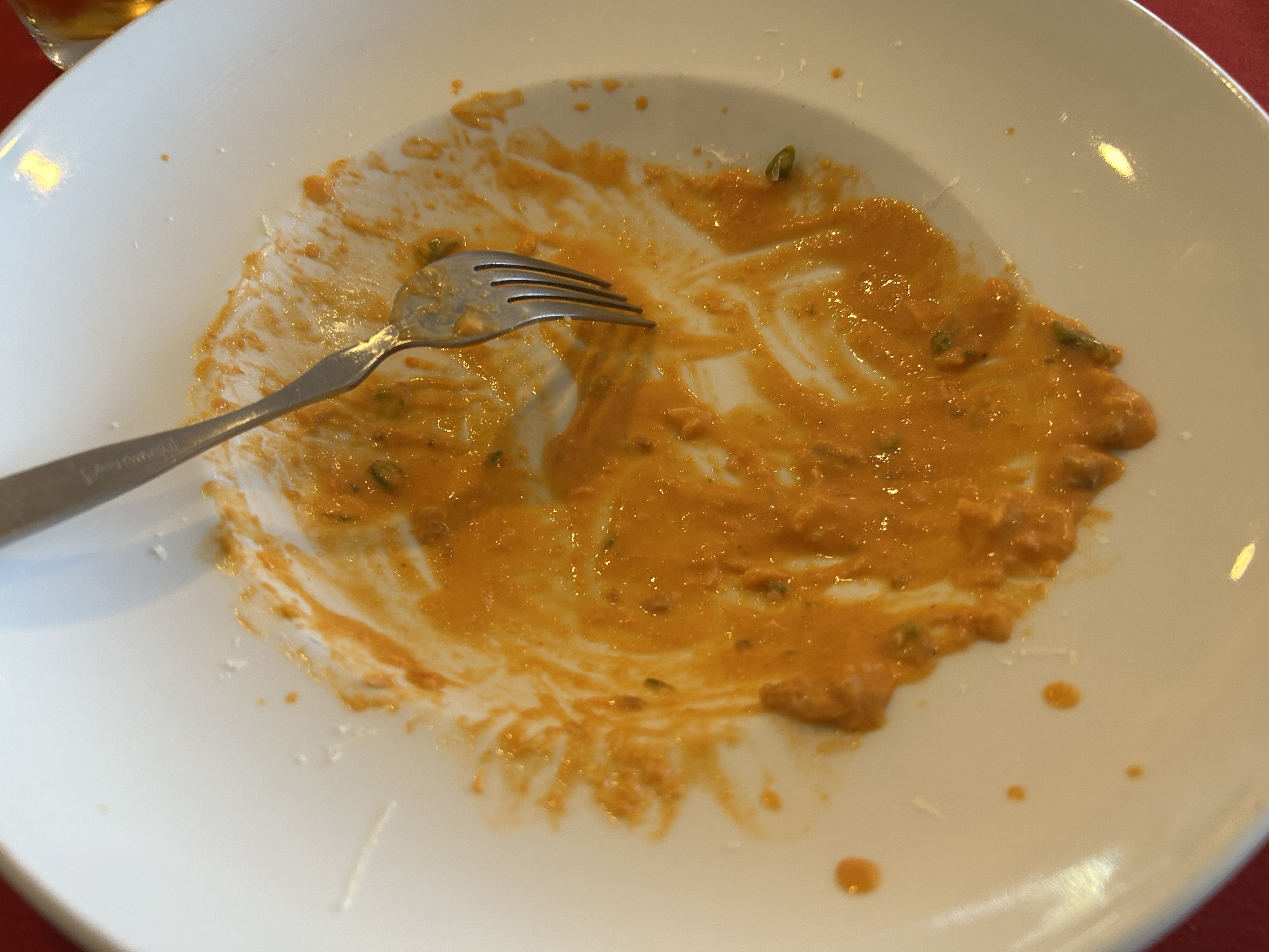 A white plate with orange curry smeared across, a fork resting in the sauce, a few green peas, and a glass in the top-left corner.