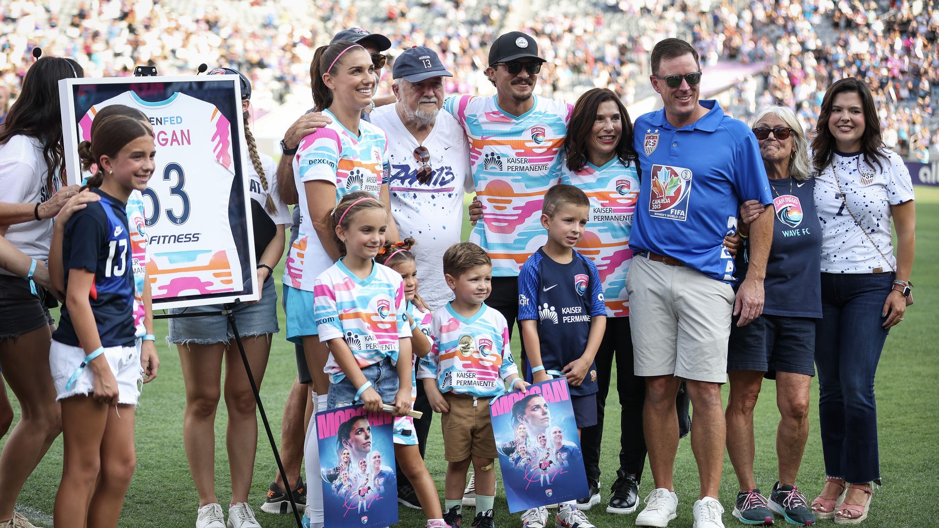 A family in tye dye shirts and a uniform stand in front of a framed jersey