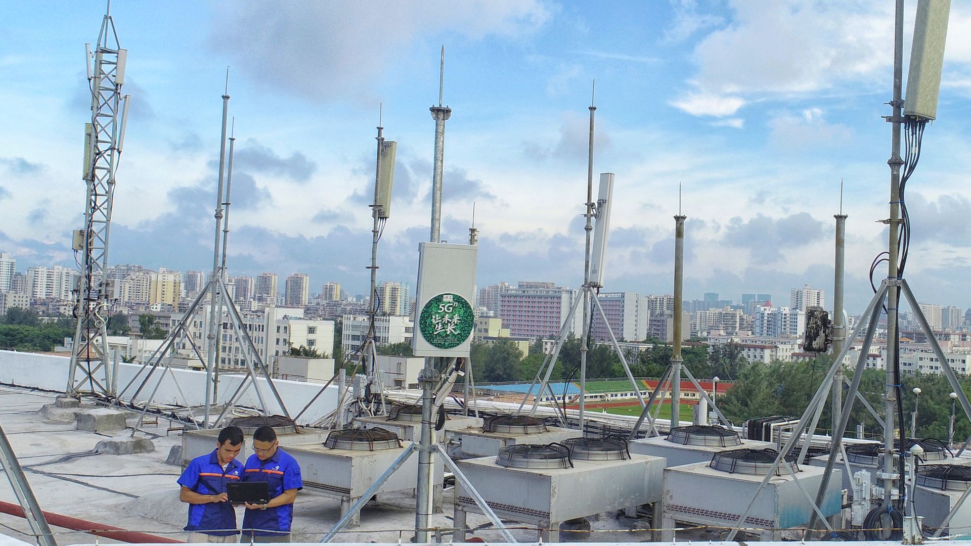 Photo of two men looking at a tablet near rooftop 5G antennas
