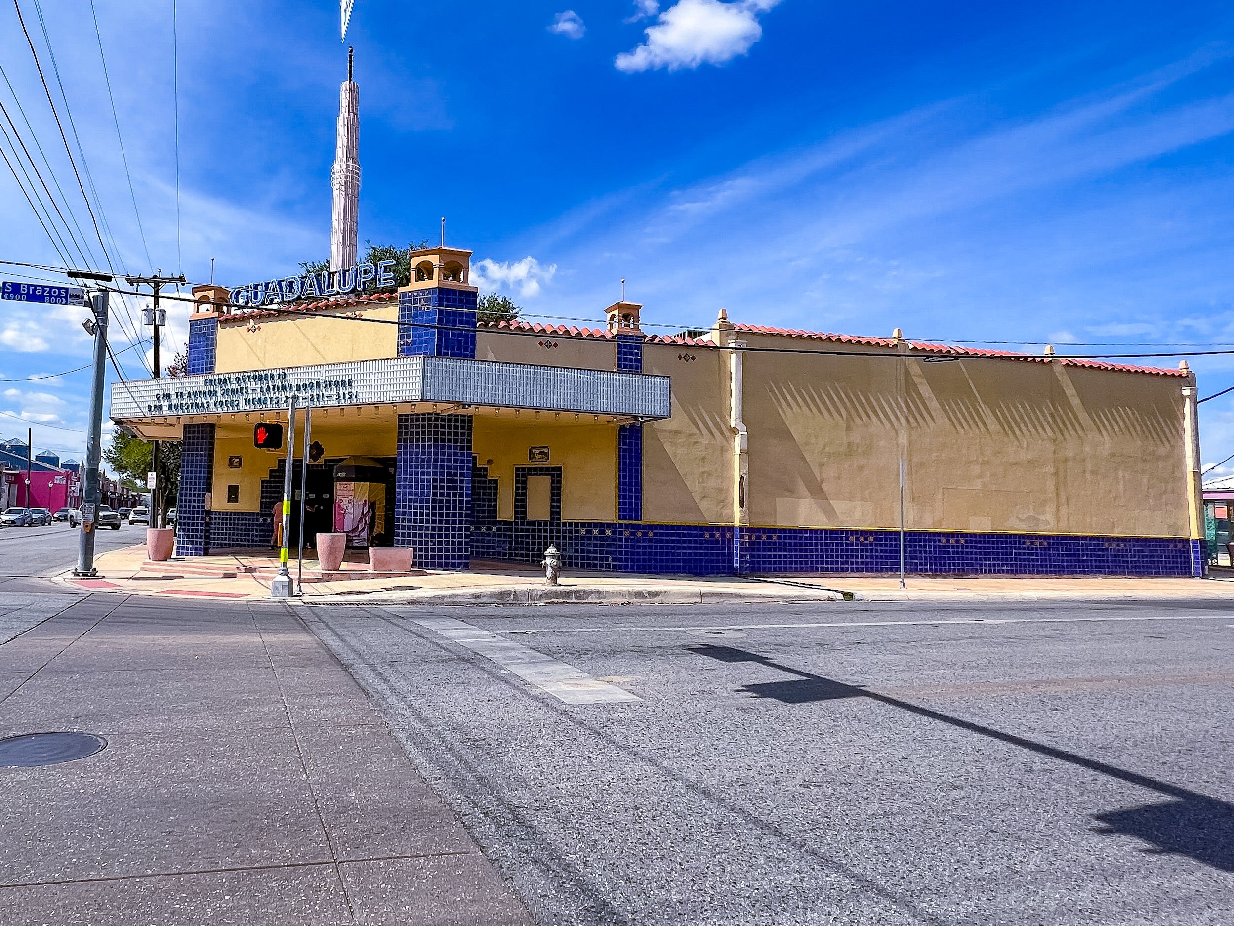 A yellow building with blue tile at a street corner with clear, blue skies behind it. 
