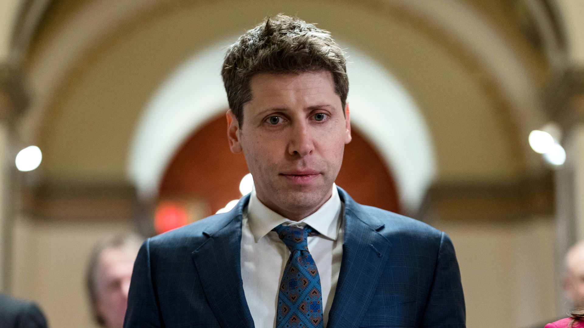 Sam Altman in a suit walking in a hallway on the House side of the U.S. Capitol 