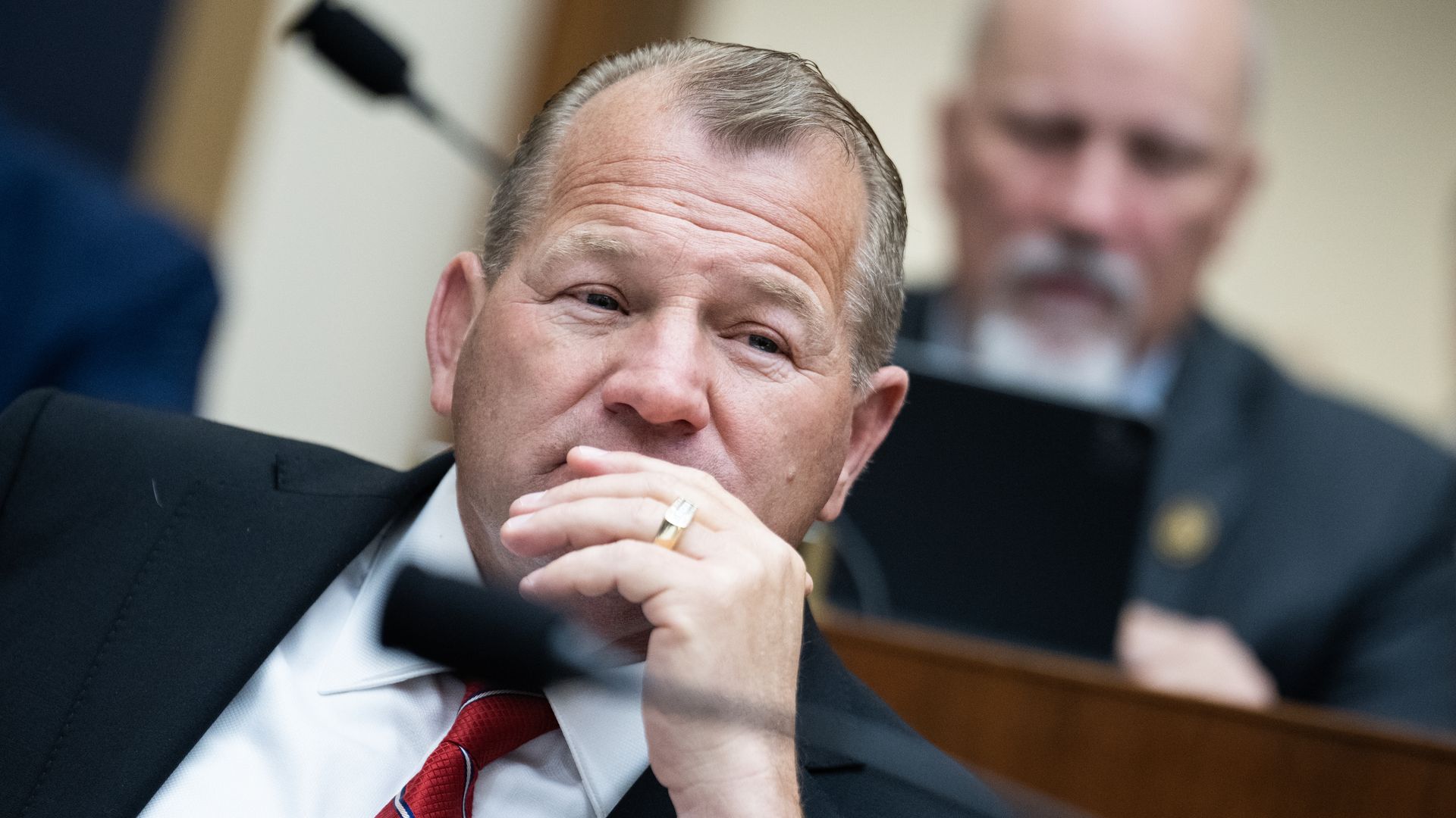Rep. Troy Nehls, wearing a dark blue suit, white shirt and red tie, sitting at a committee hearing.