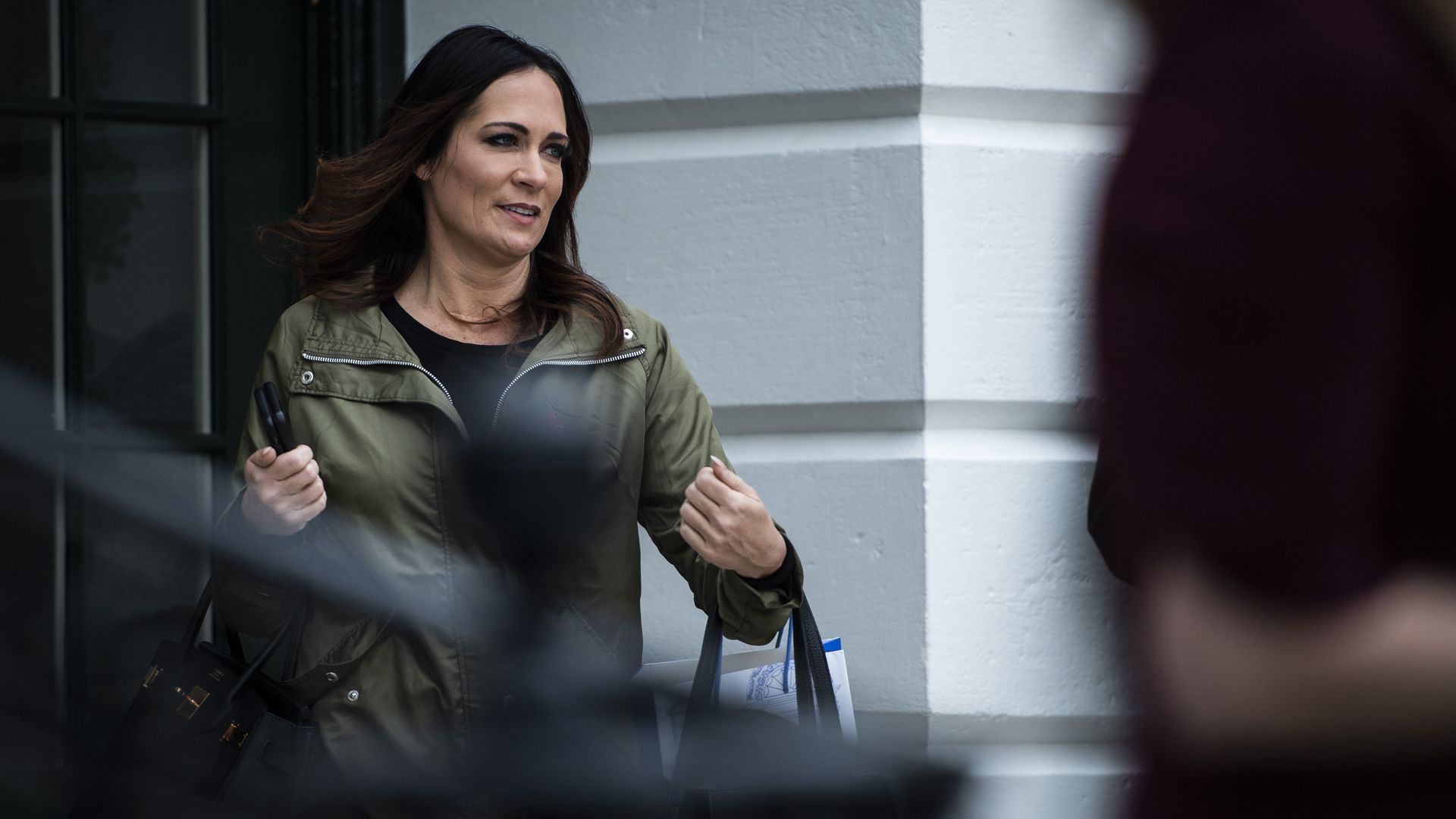 In this image, Stephanie walks out of a doorway while carrying a bag.