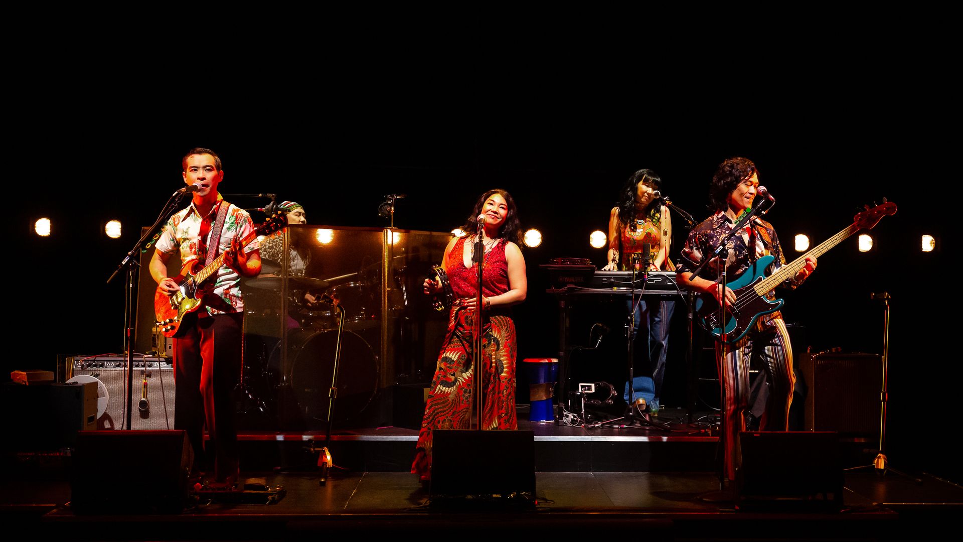Photo of a group of people performing on stage, dressed in 70s attire. 