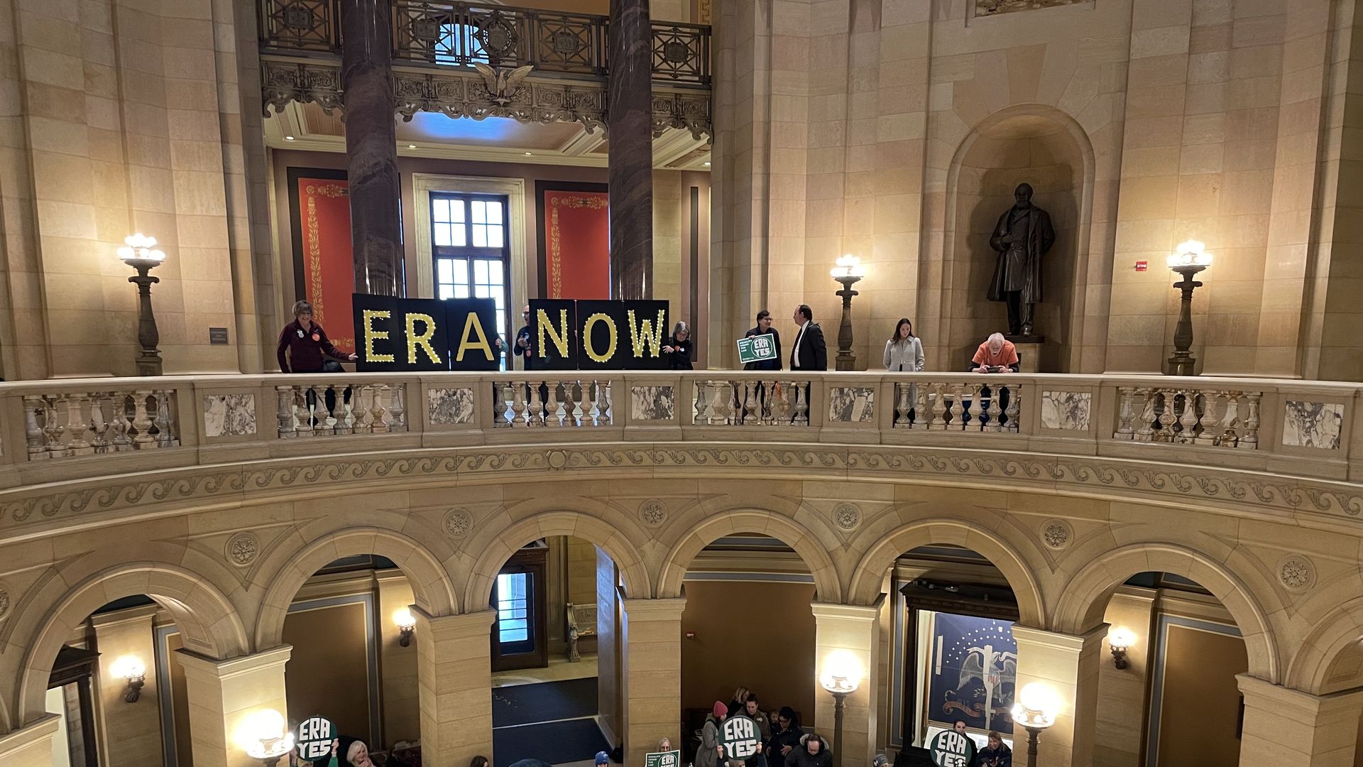 people hold a sign sqying ERA now on the second floor of the rodunda of the state capitol