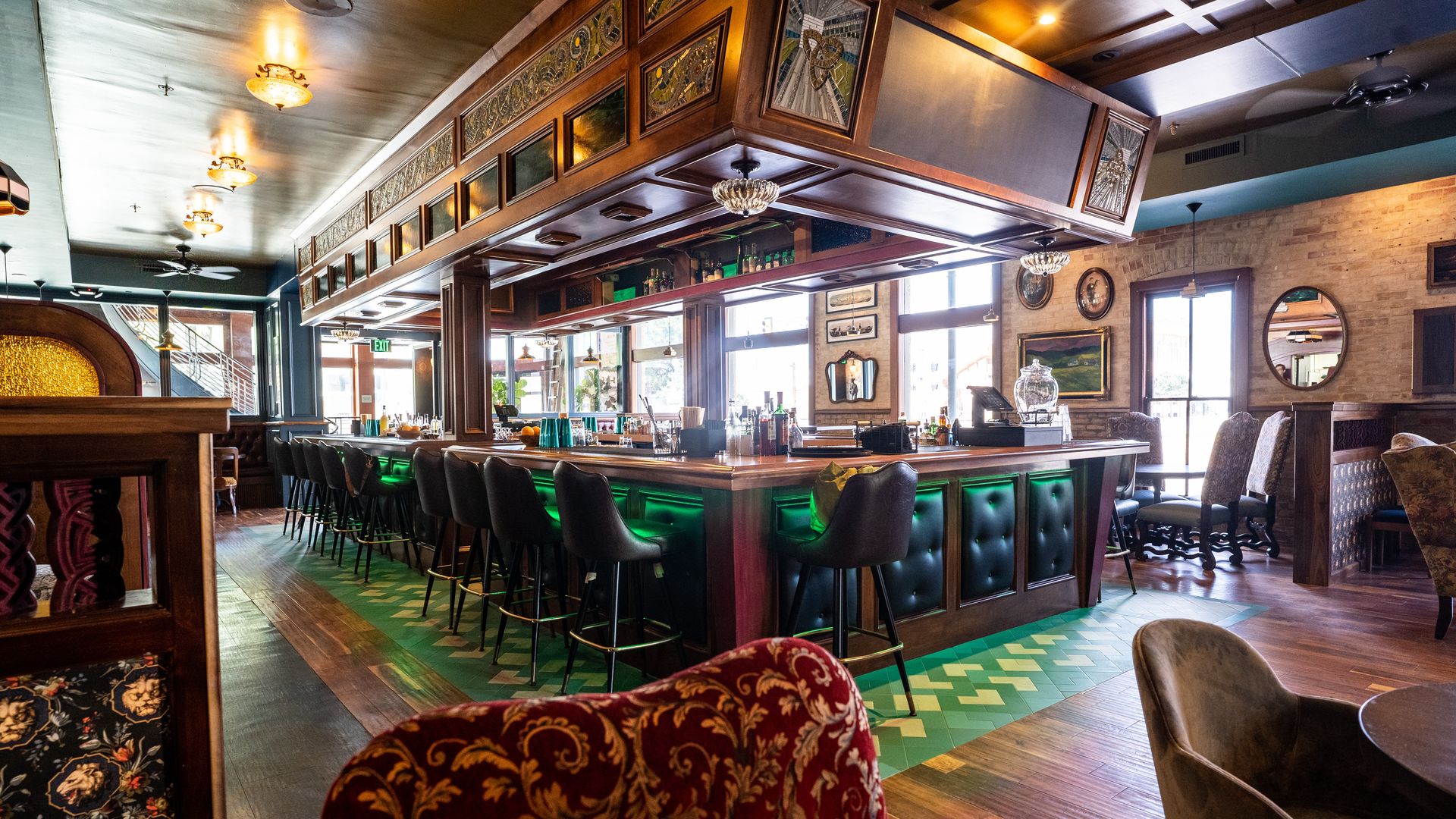 A wooden bar with leather accents surrounded by black bar stools.