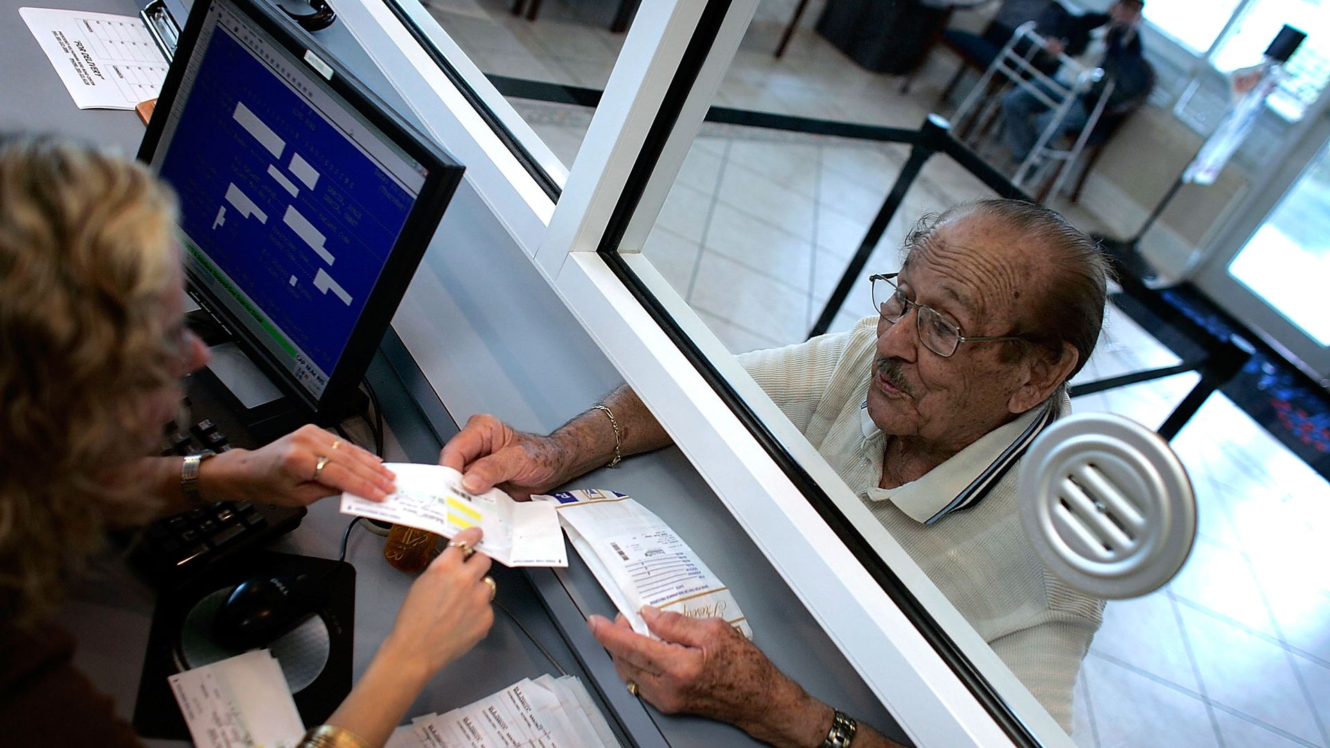 An older man grabs his prescription drugs at a pharmacy counter.