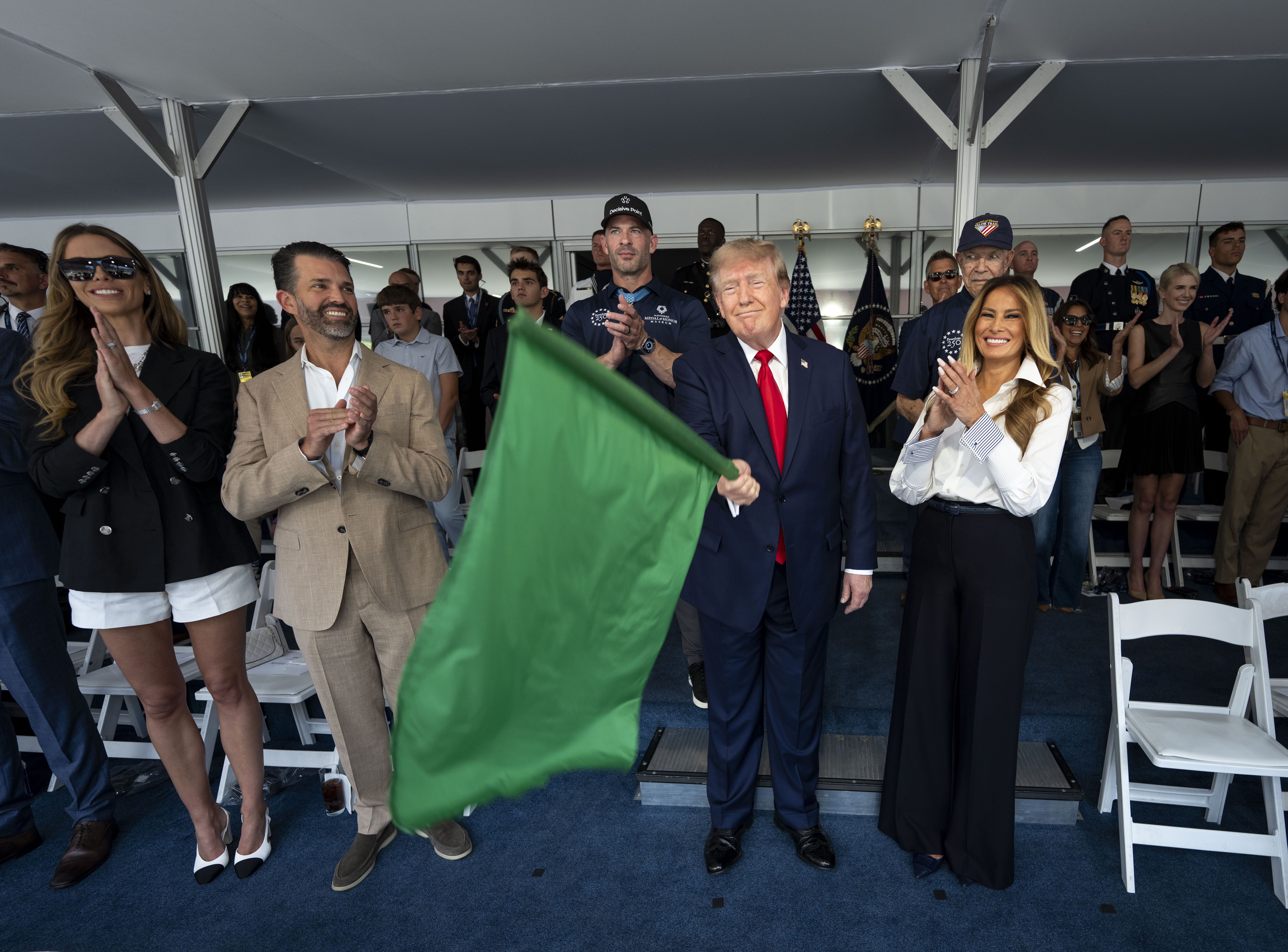 President Donald Trump waves the green flag to start the race next to first lady Melania Trump and Donald Trump Jr. 